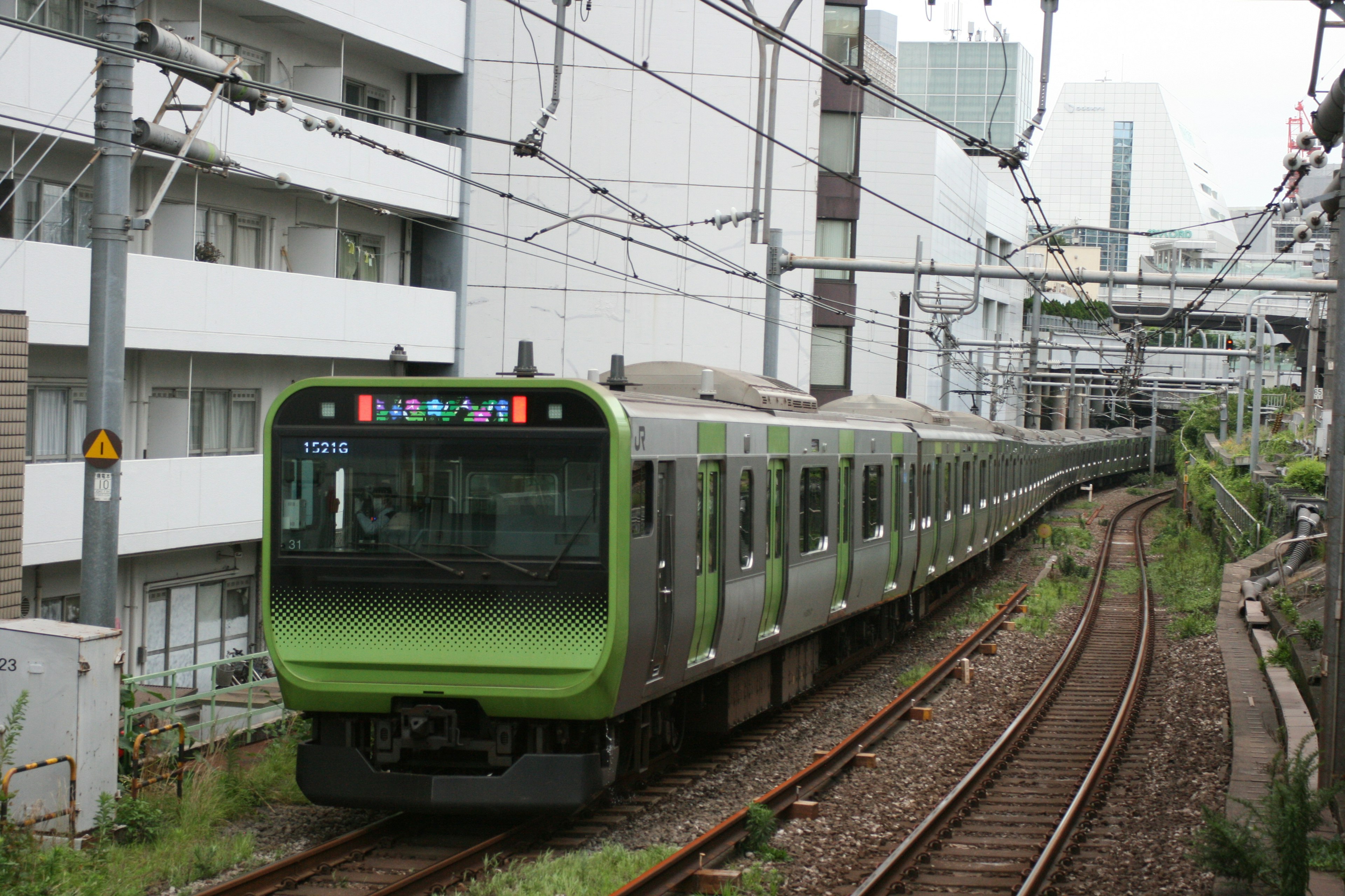 Tren verde viajando por las vías con edificios de fondo