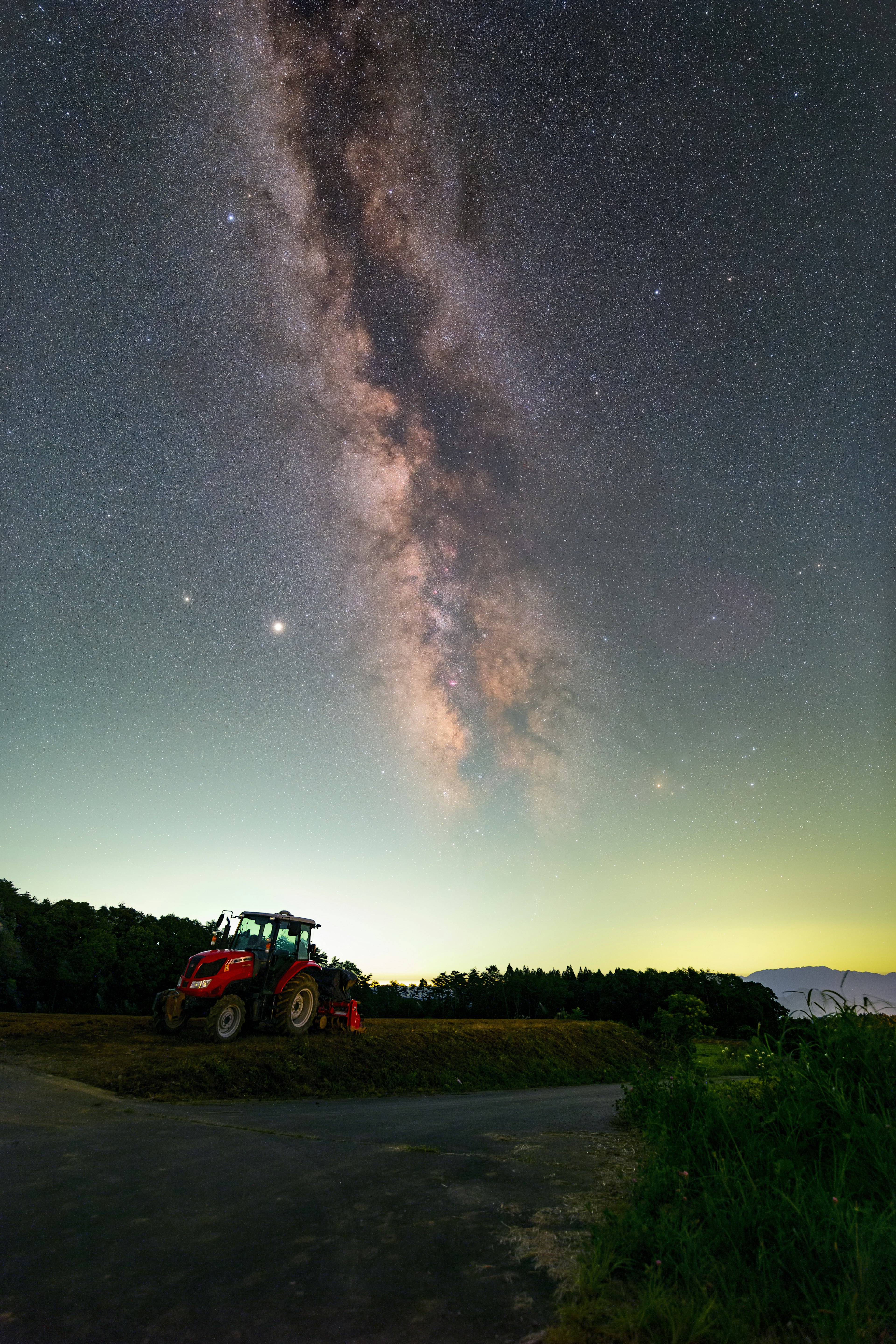 星空の下に立つ赤いトラクターと天の川