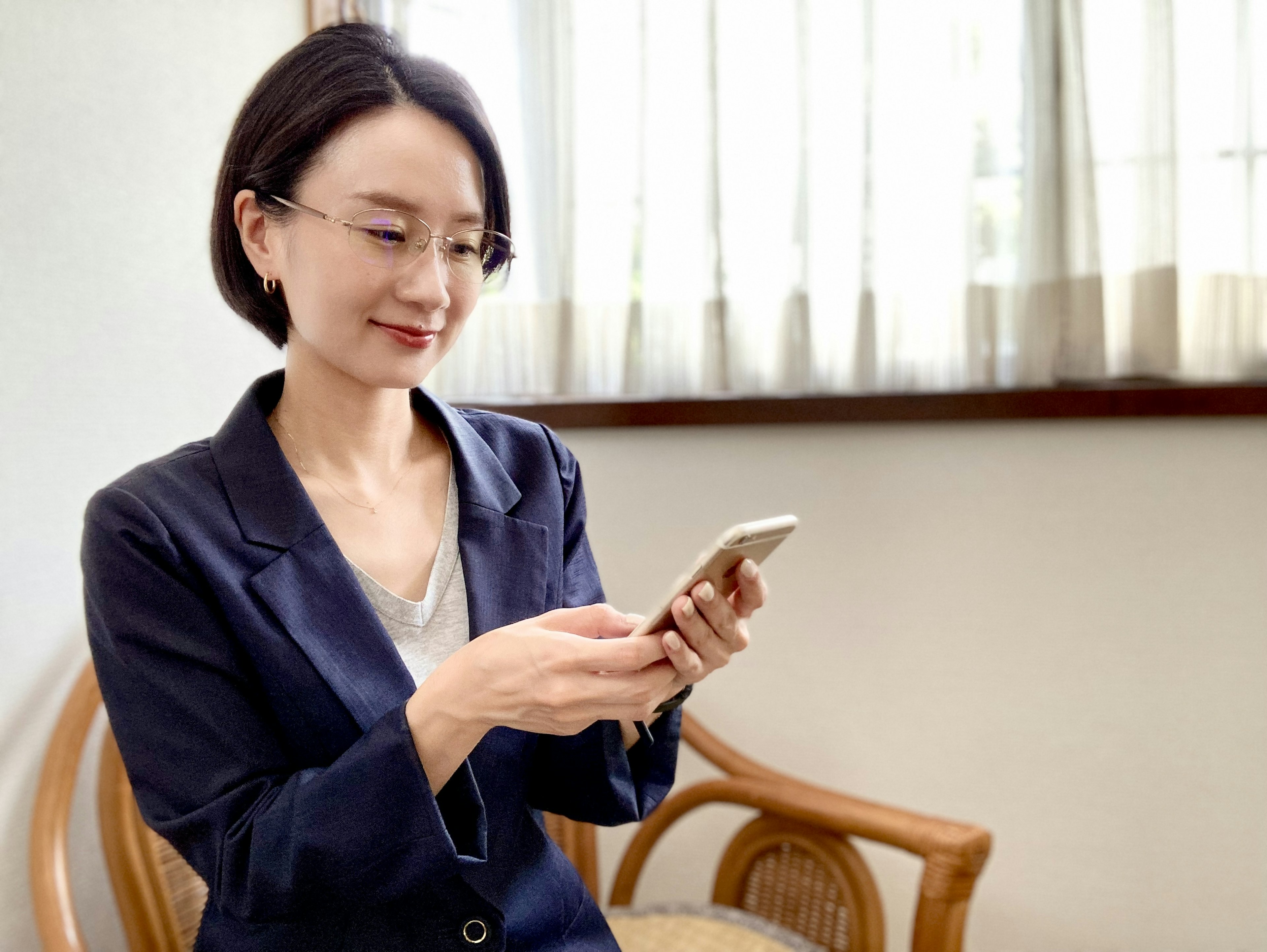 A woman using a smartphone while sitting in a chair with a slight smile