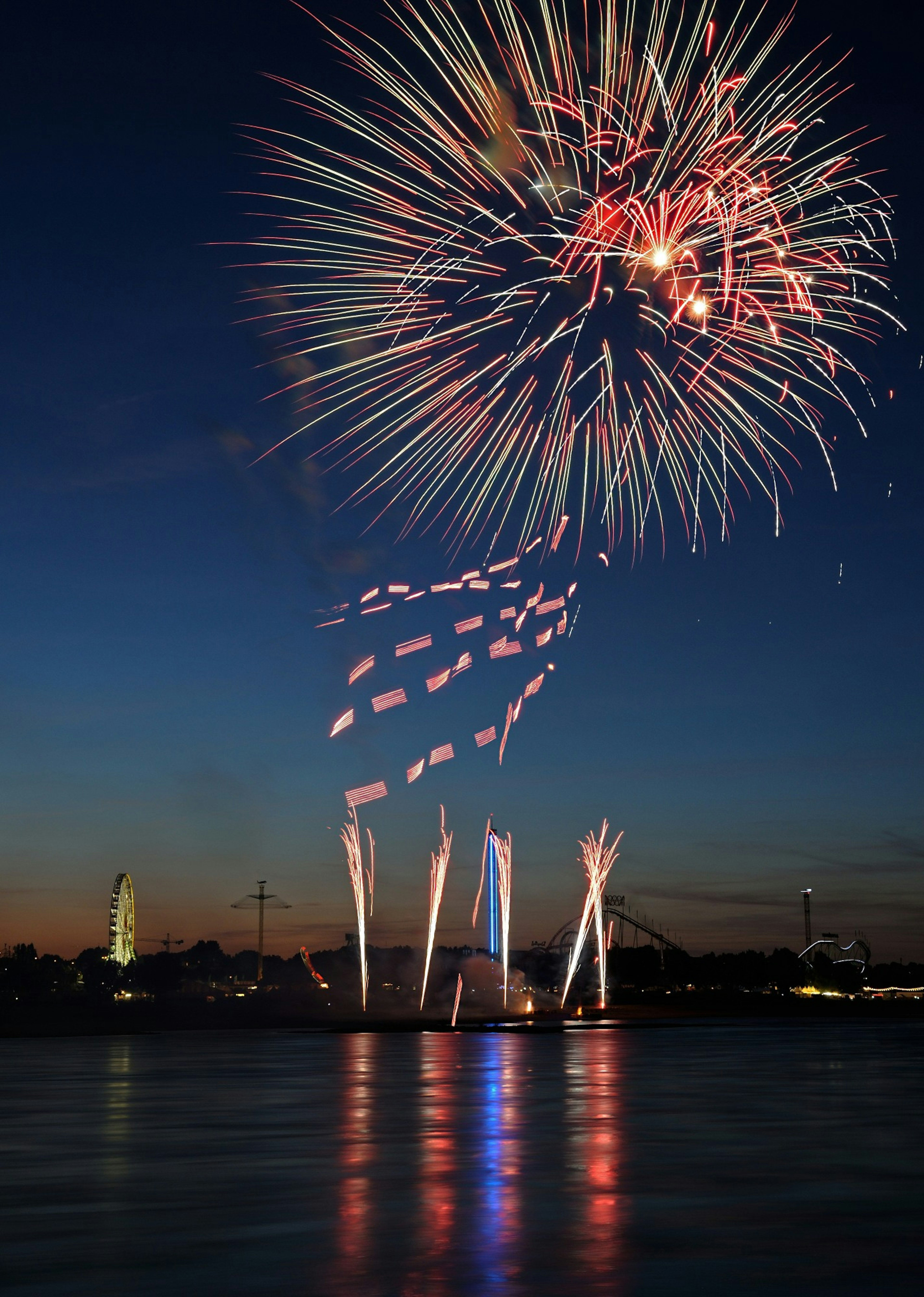 Colorful fireworks display over a calm body of water at dusk