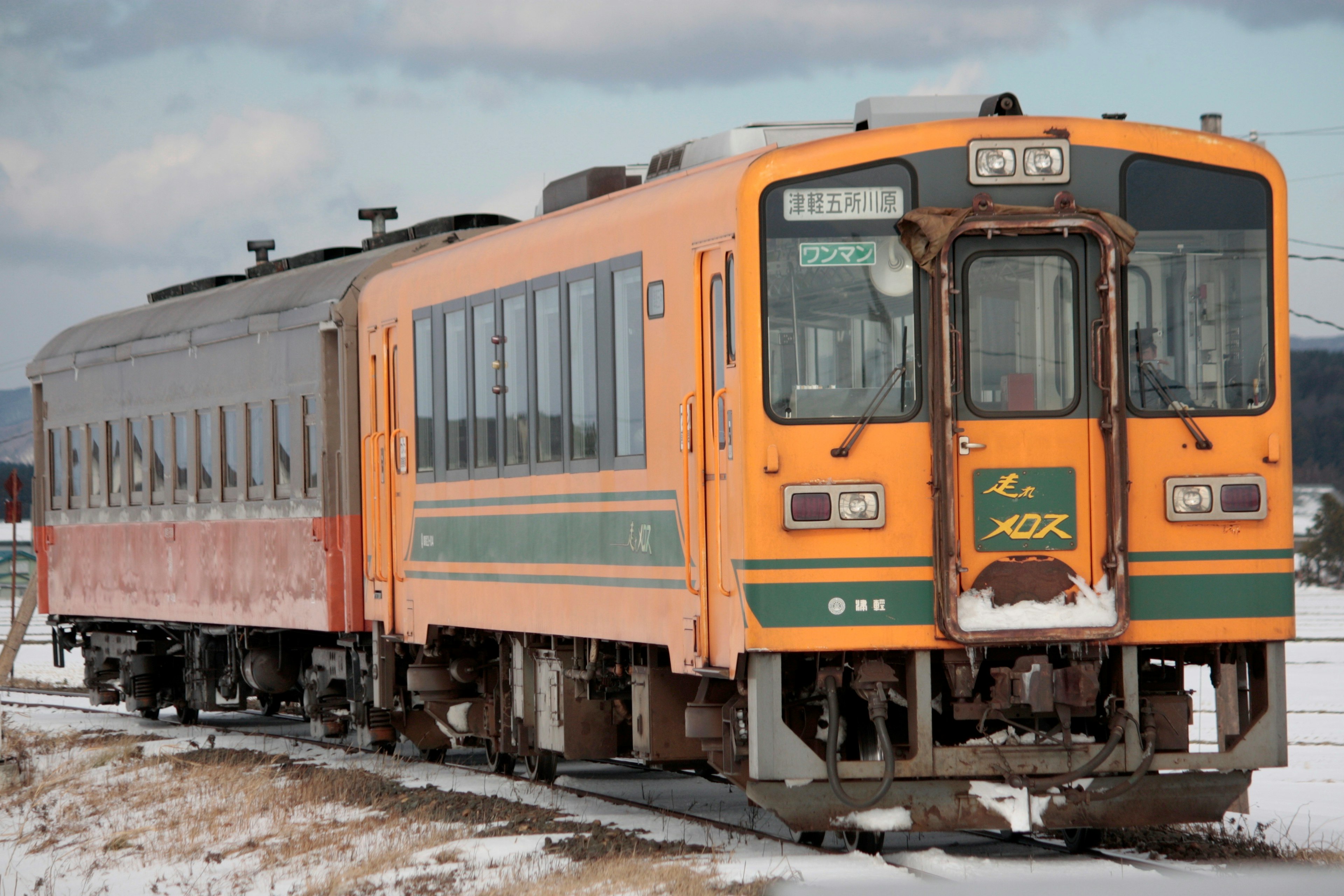 Un train orange avec un wagon passager rouge circulant sur des rails enneigés