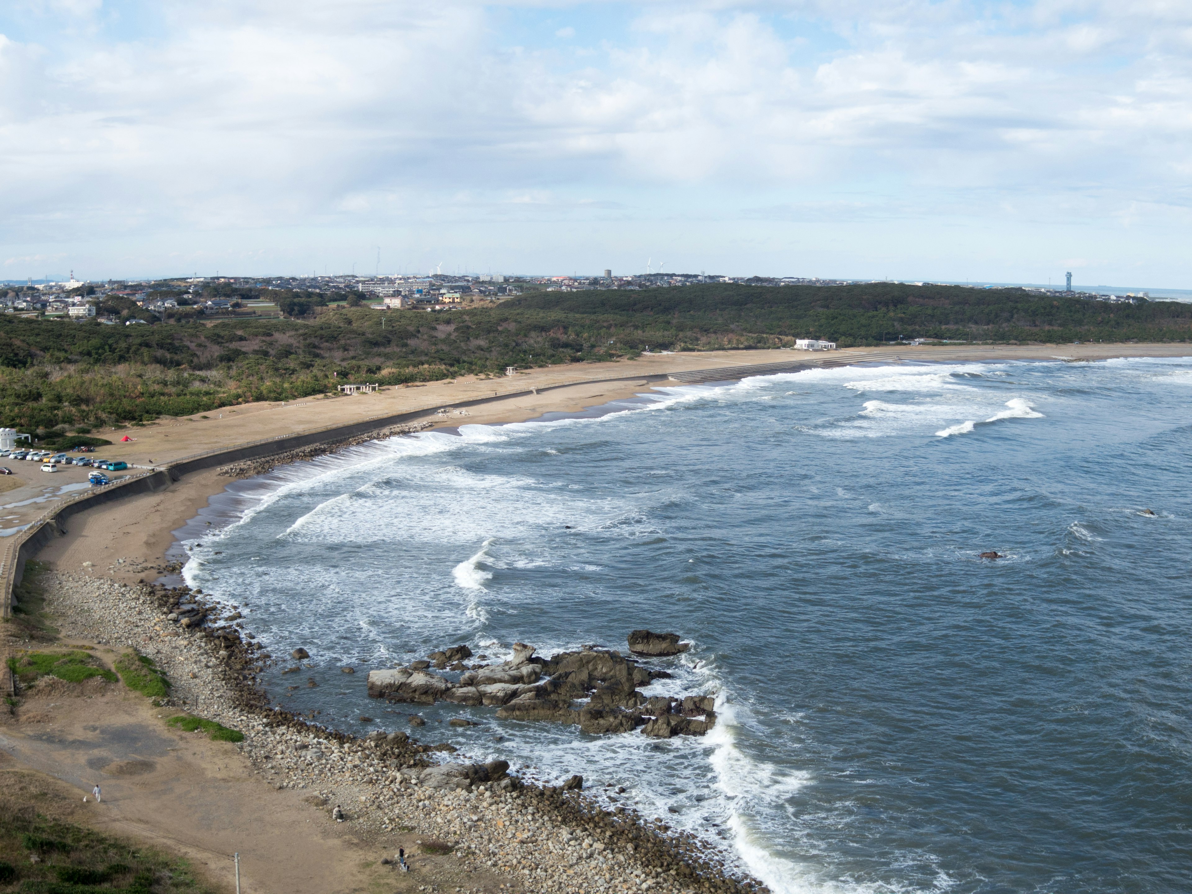 Vista costiera con spiaggia sabbiosa, onde, costa rocciosa e cielo sereno