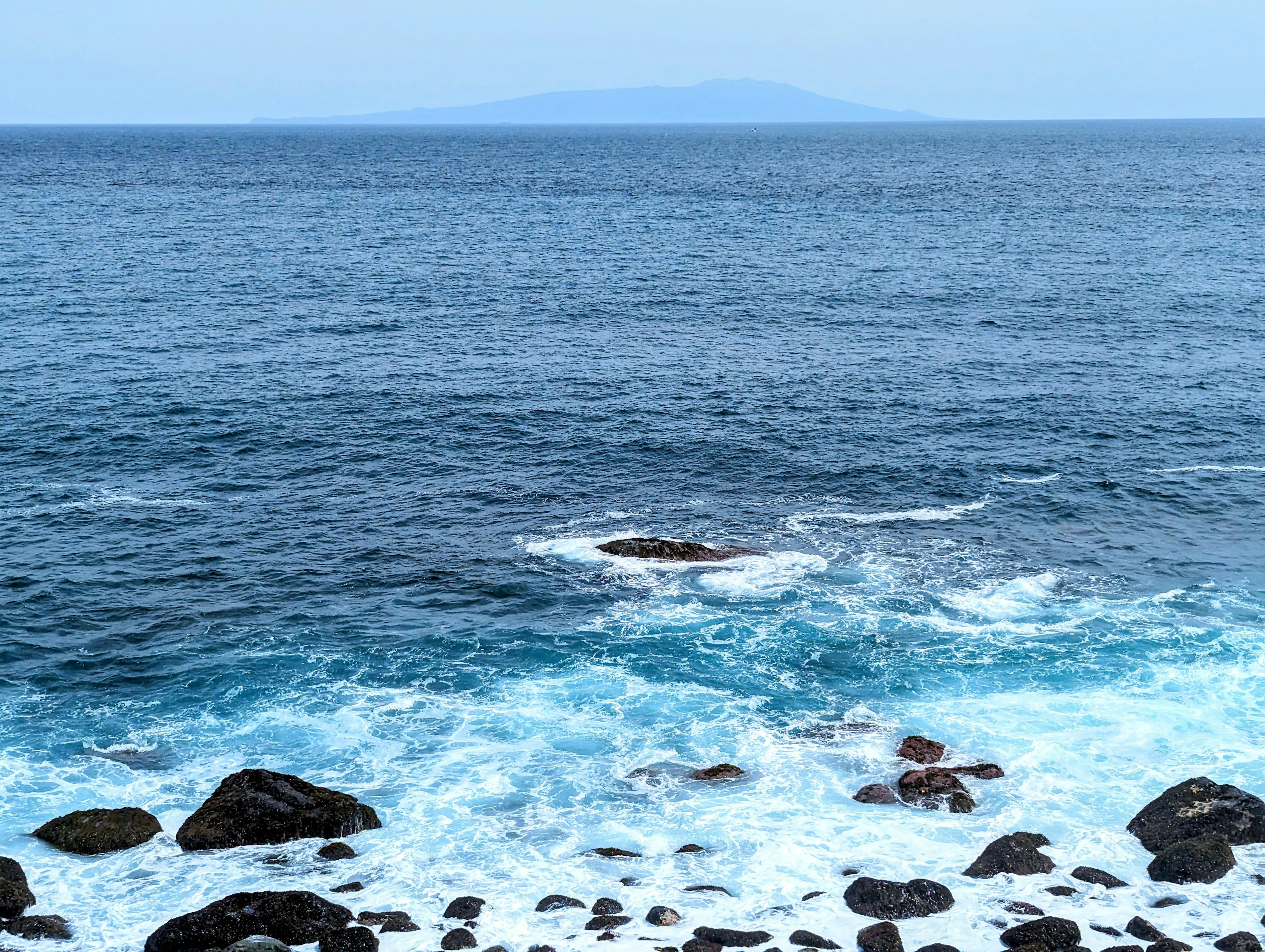 Vista panoramica dell'oceano blu con rocce e un'isola lontana