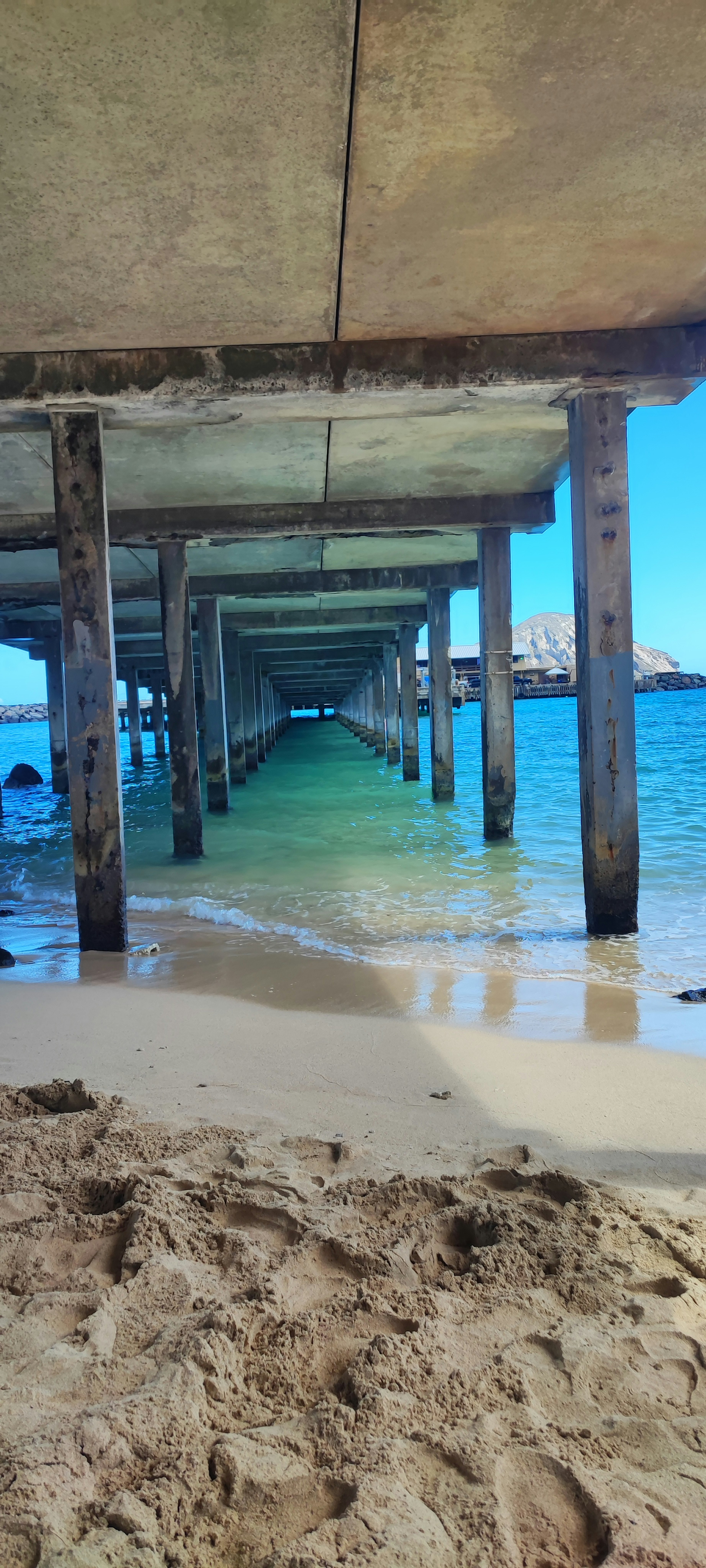 Di bawah dermaga dengan tiang kayu dan air biru jernih