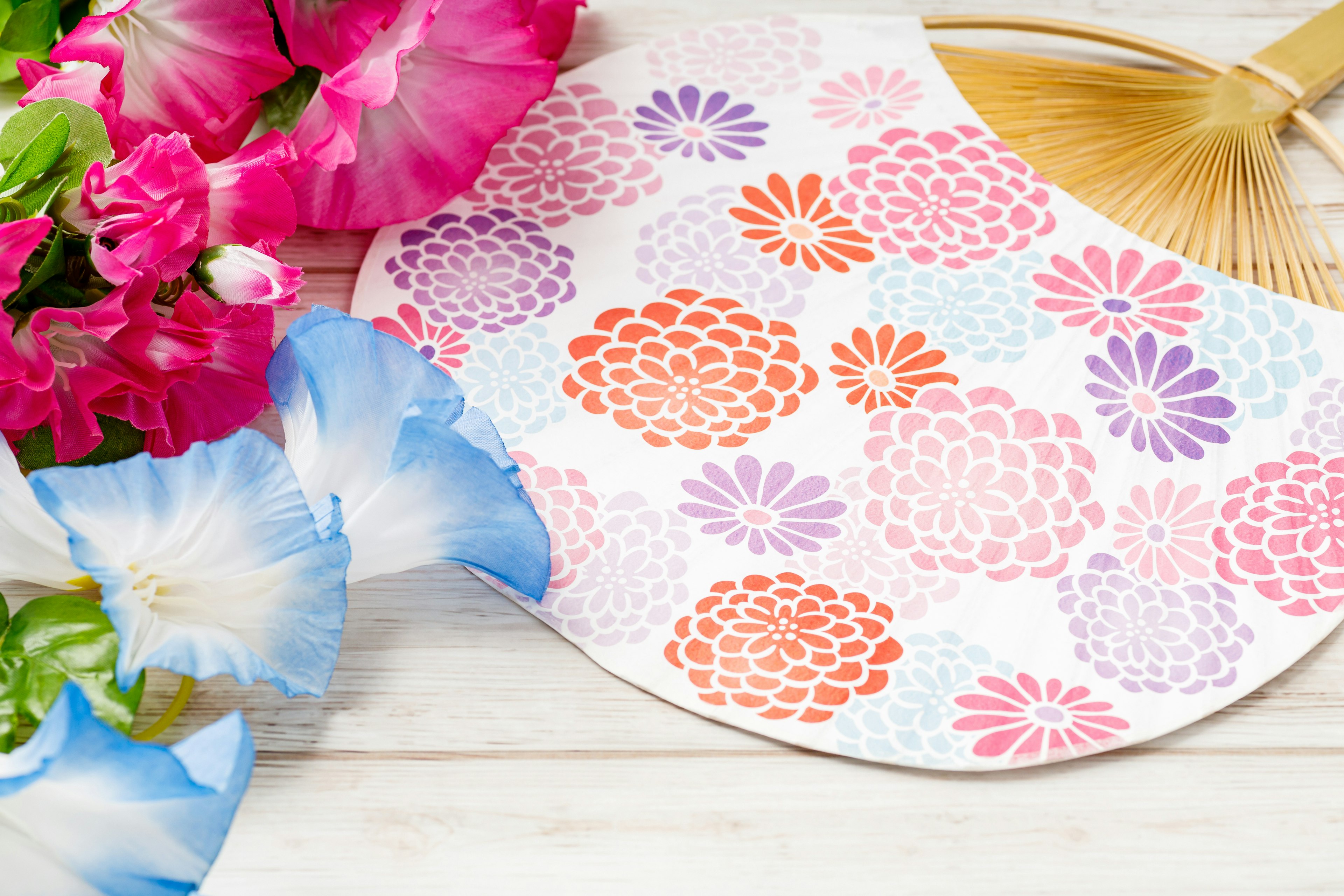 Colorful floral patterned fan beside a bouquet of flowers on a wooden surface