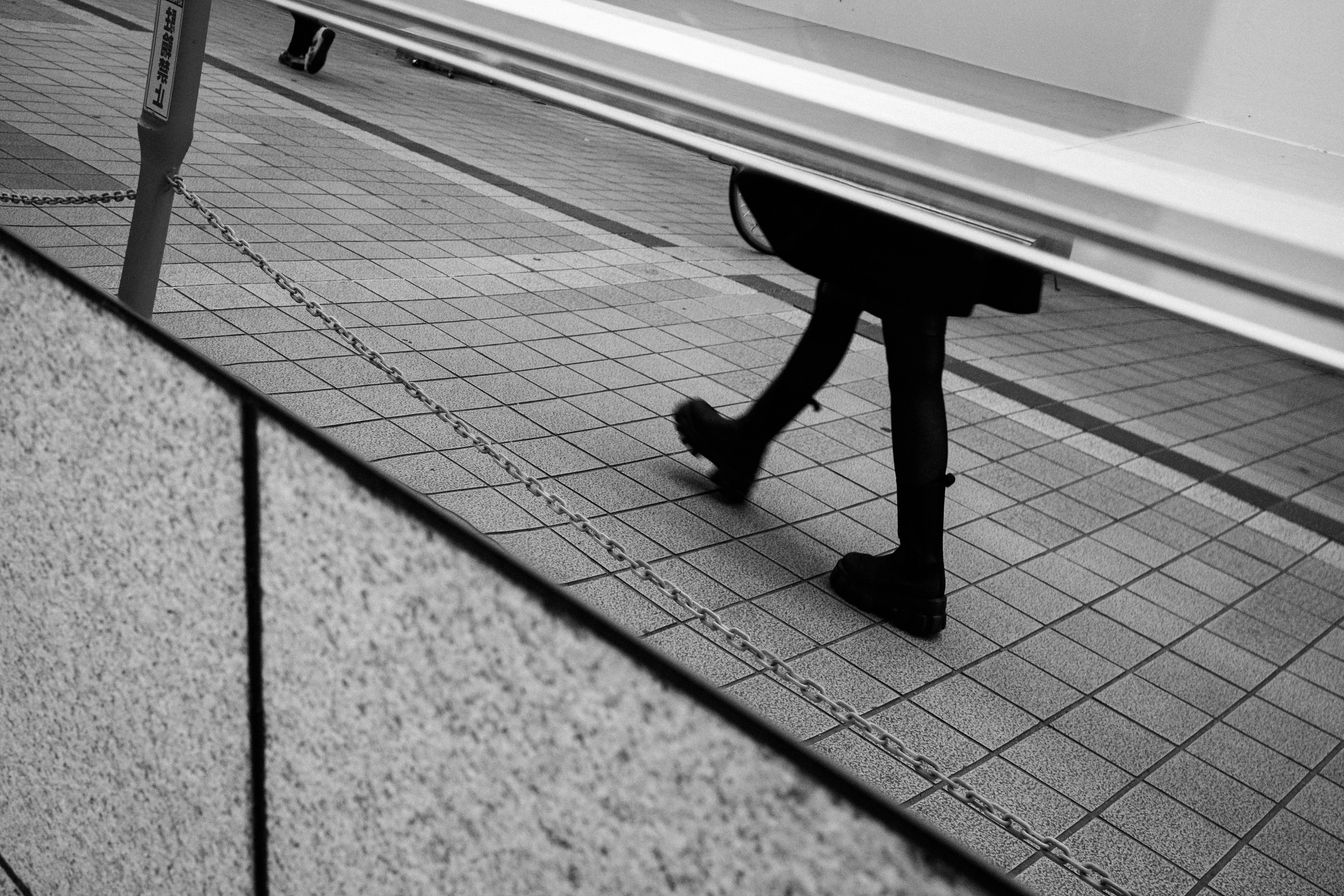 Black and white street scene featuring a person's legs walking