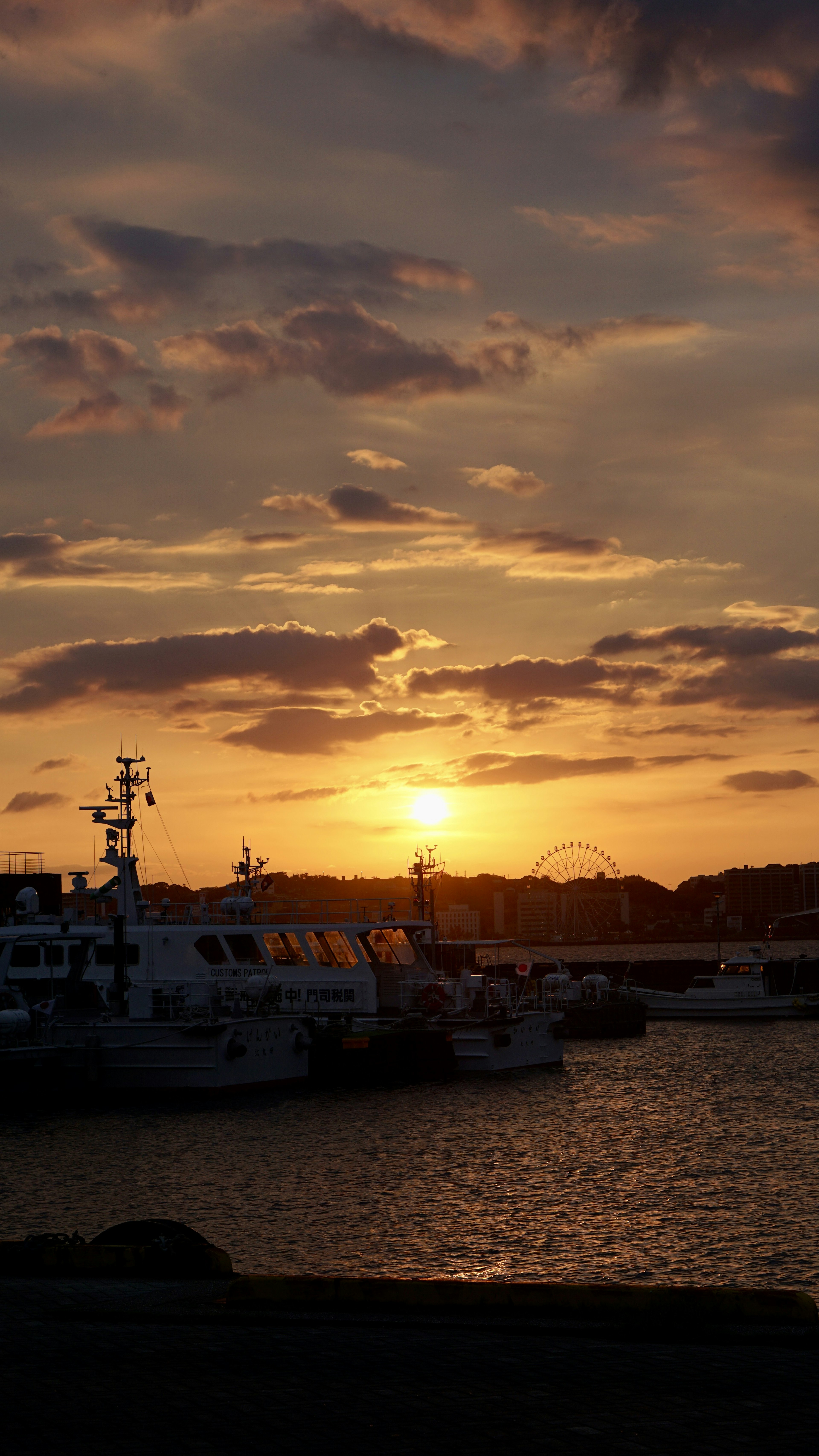 Harbor scene at sunset with boats reflecting orange light on the water