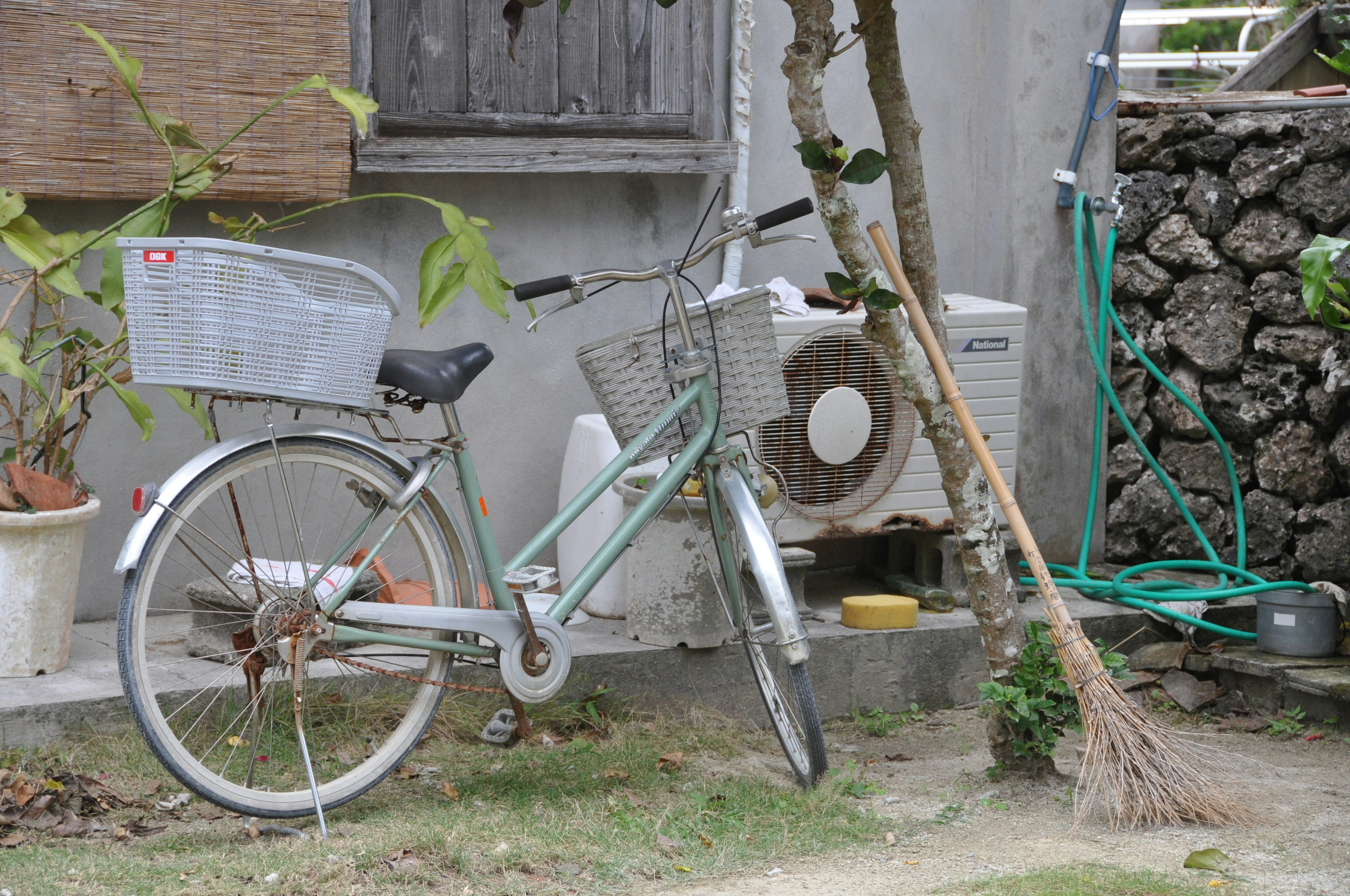 Una bicicletta verde parcheggiata all'esterno con un condizionatore e piante sullo sfondo