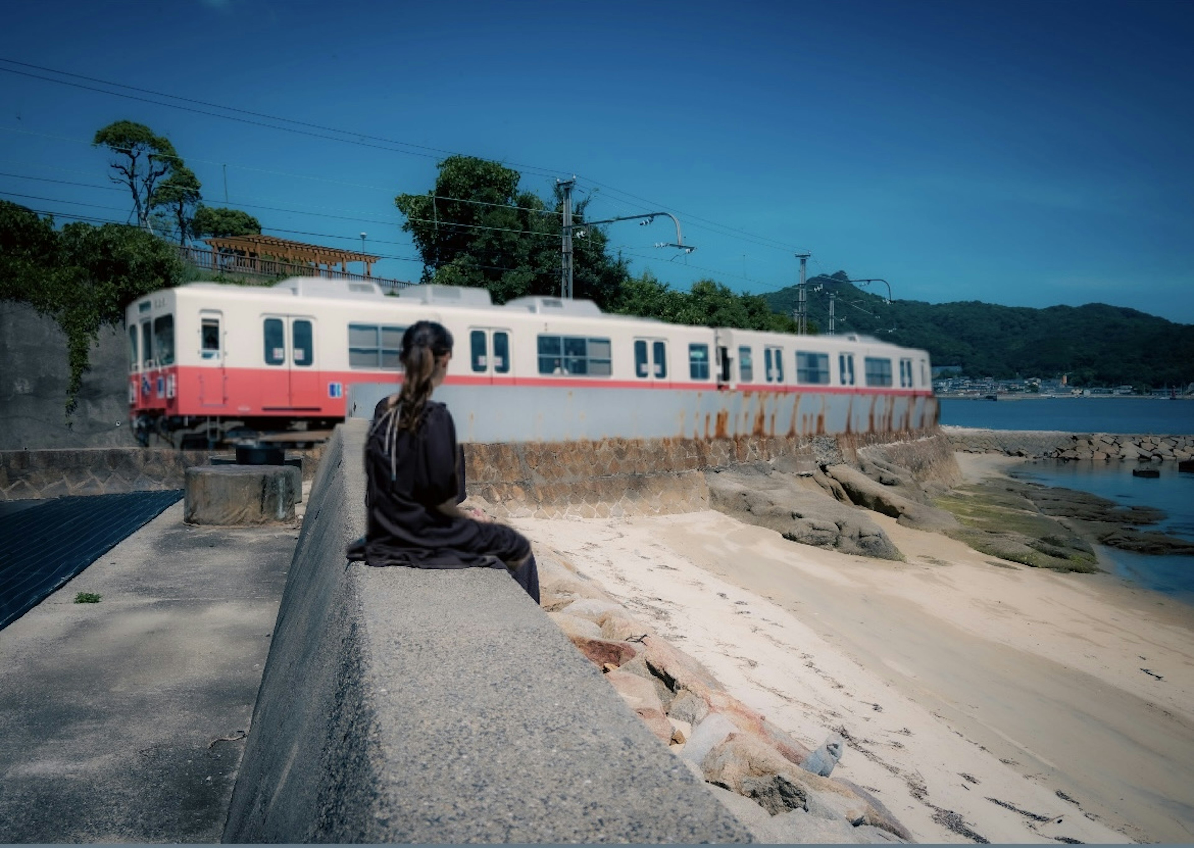 Une femme assise au bord de la voie ferrée en bord de mer avec un vieux train