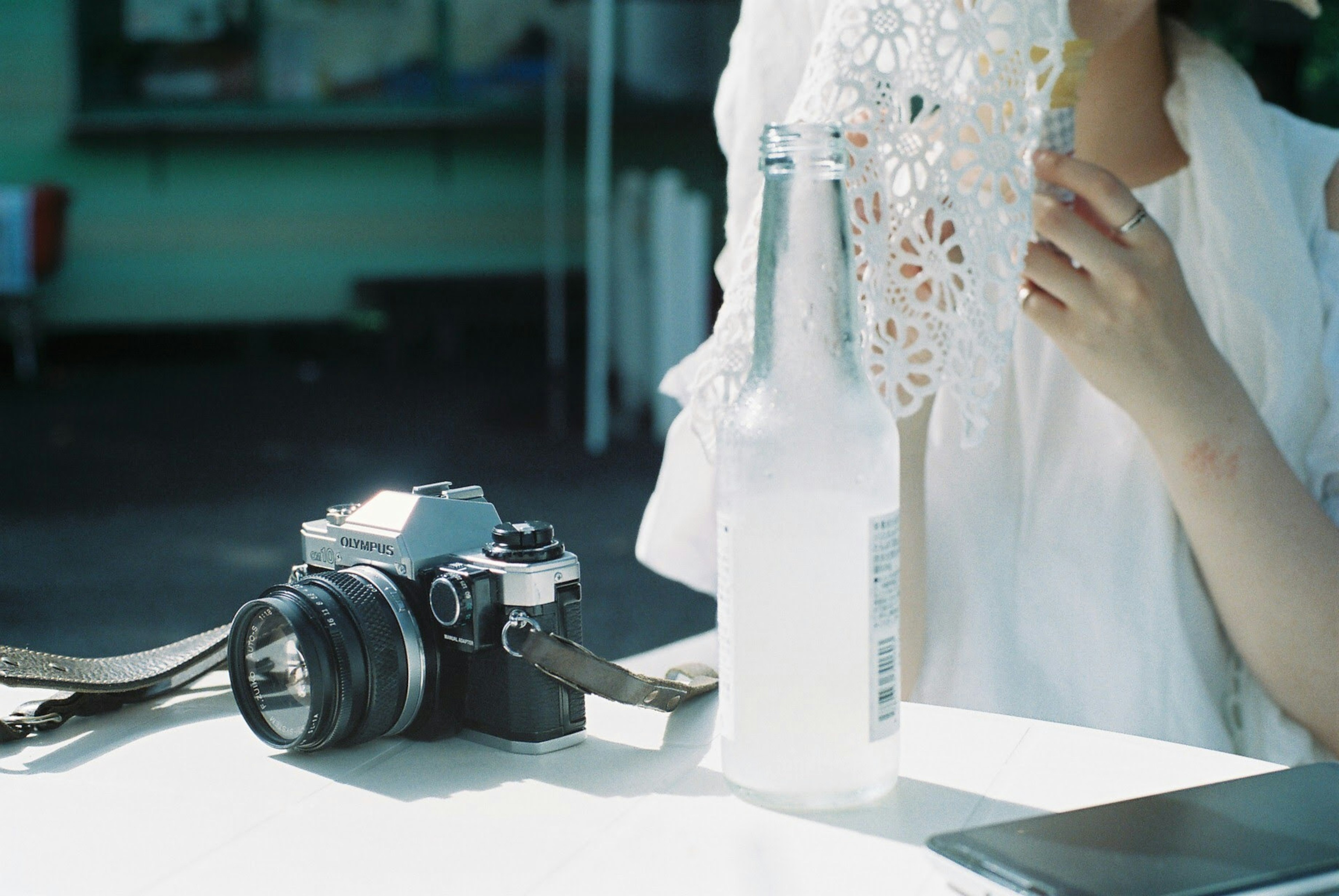 A woman in white clothing sitting at a table with a camera and a drink