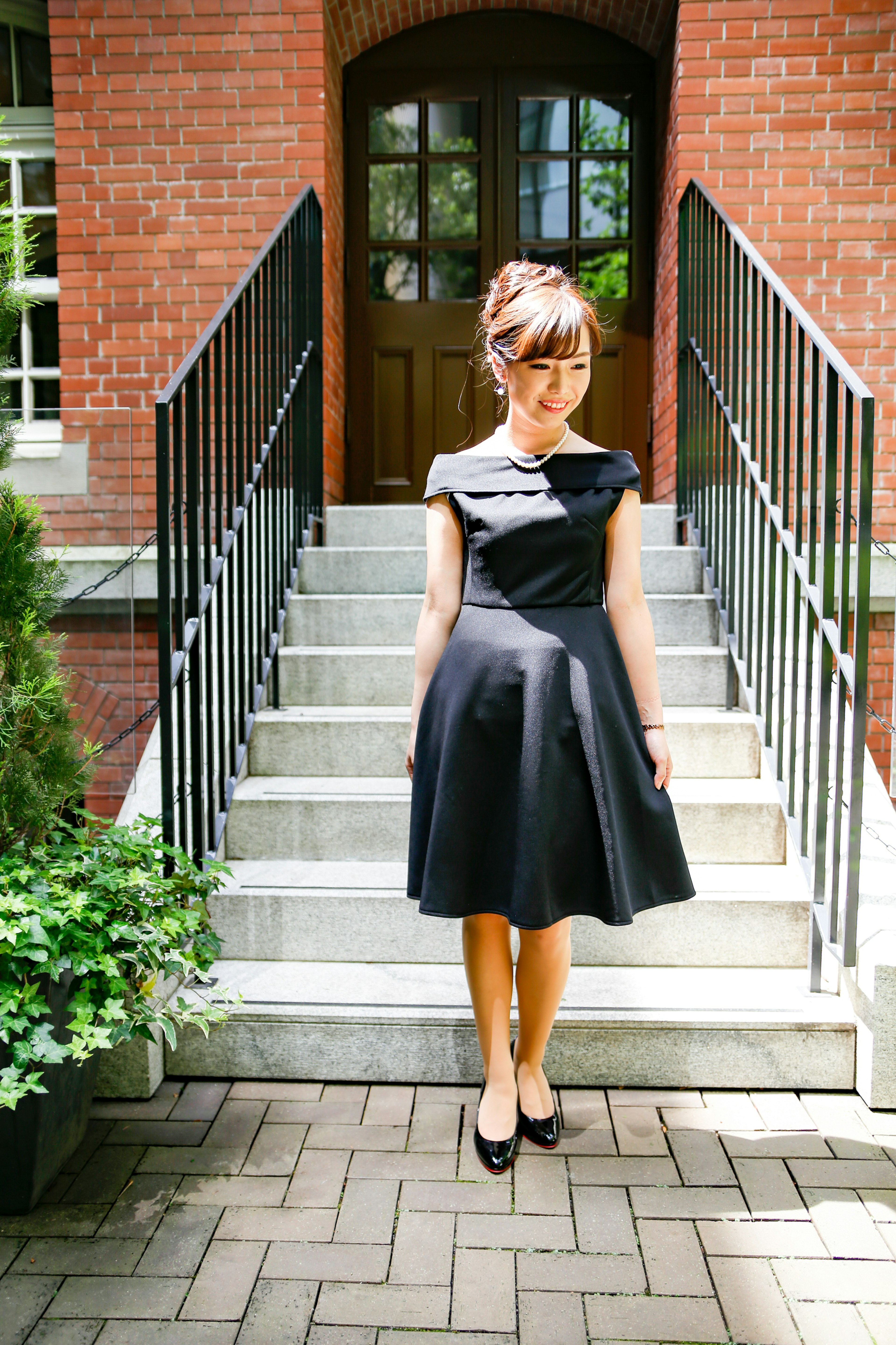 A woman in a black dress standing in front of stairs