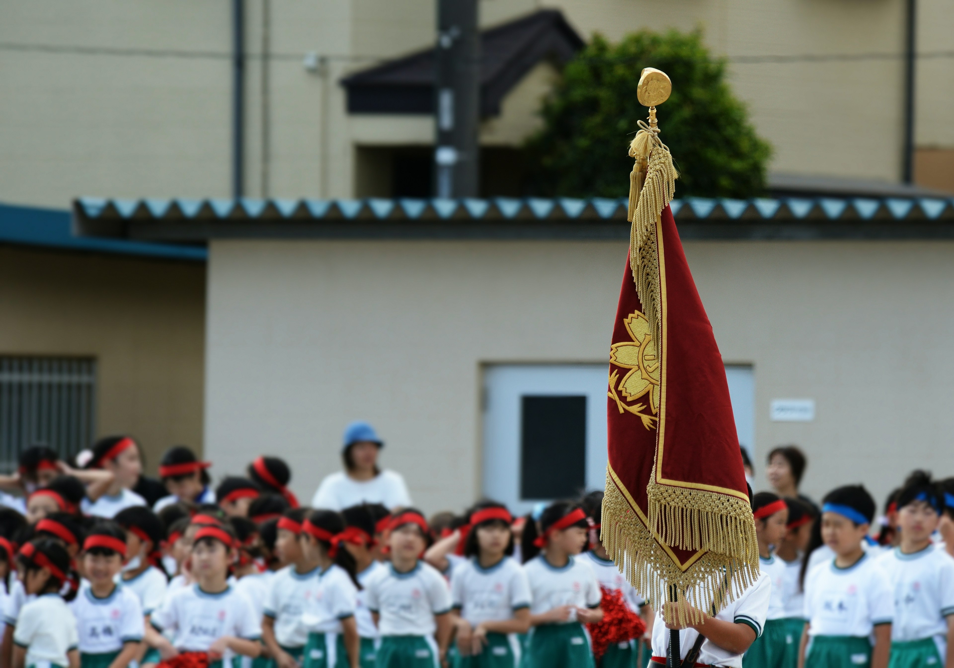 Reunión de niños en un día deportivo sosteniendo una bandera con un edificio escolar al fondo