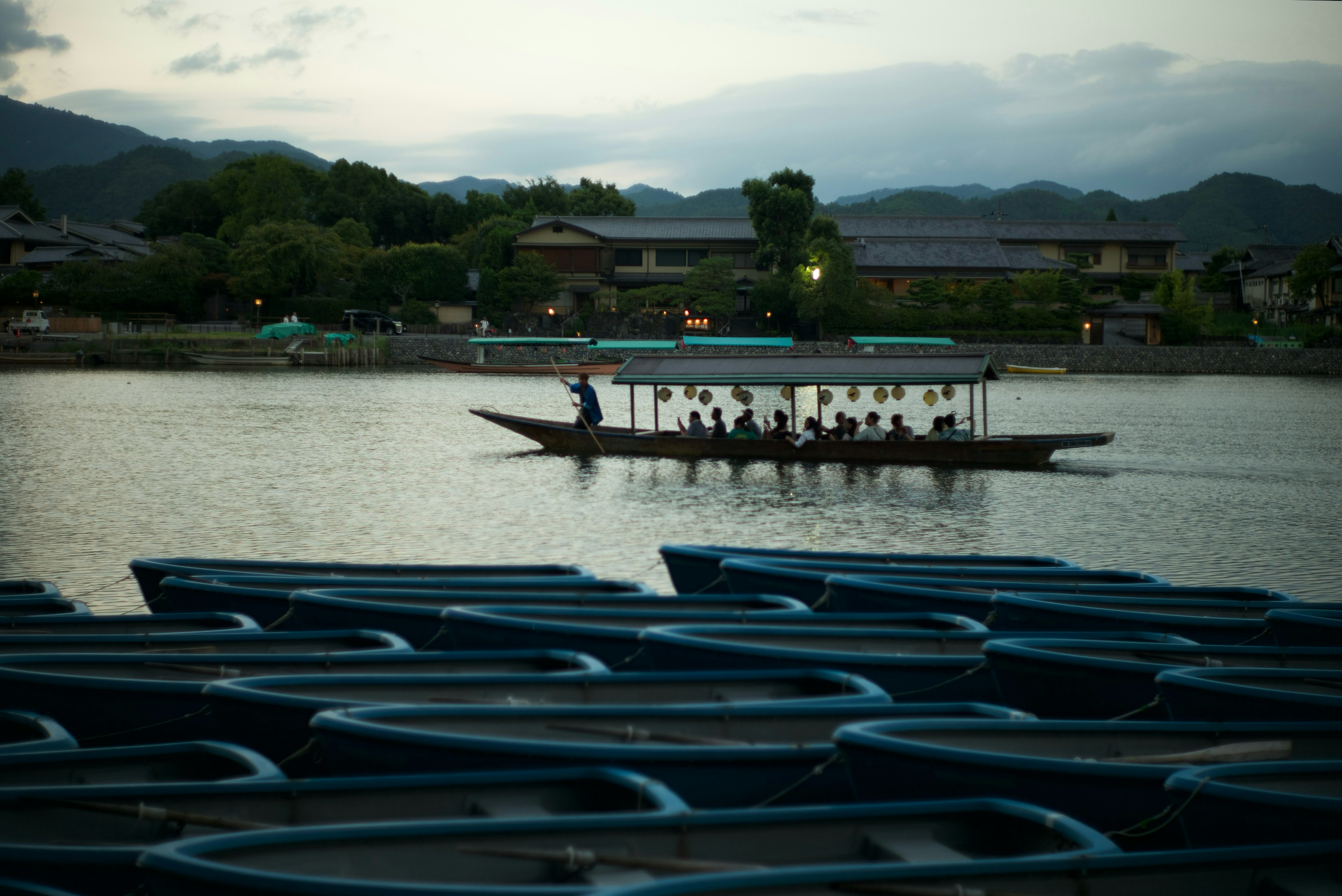 A scenic view of a boat moving on a lake at dusk with a line of blue boats in the foreground