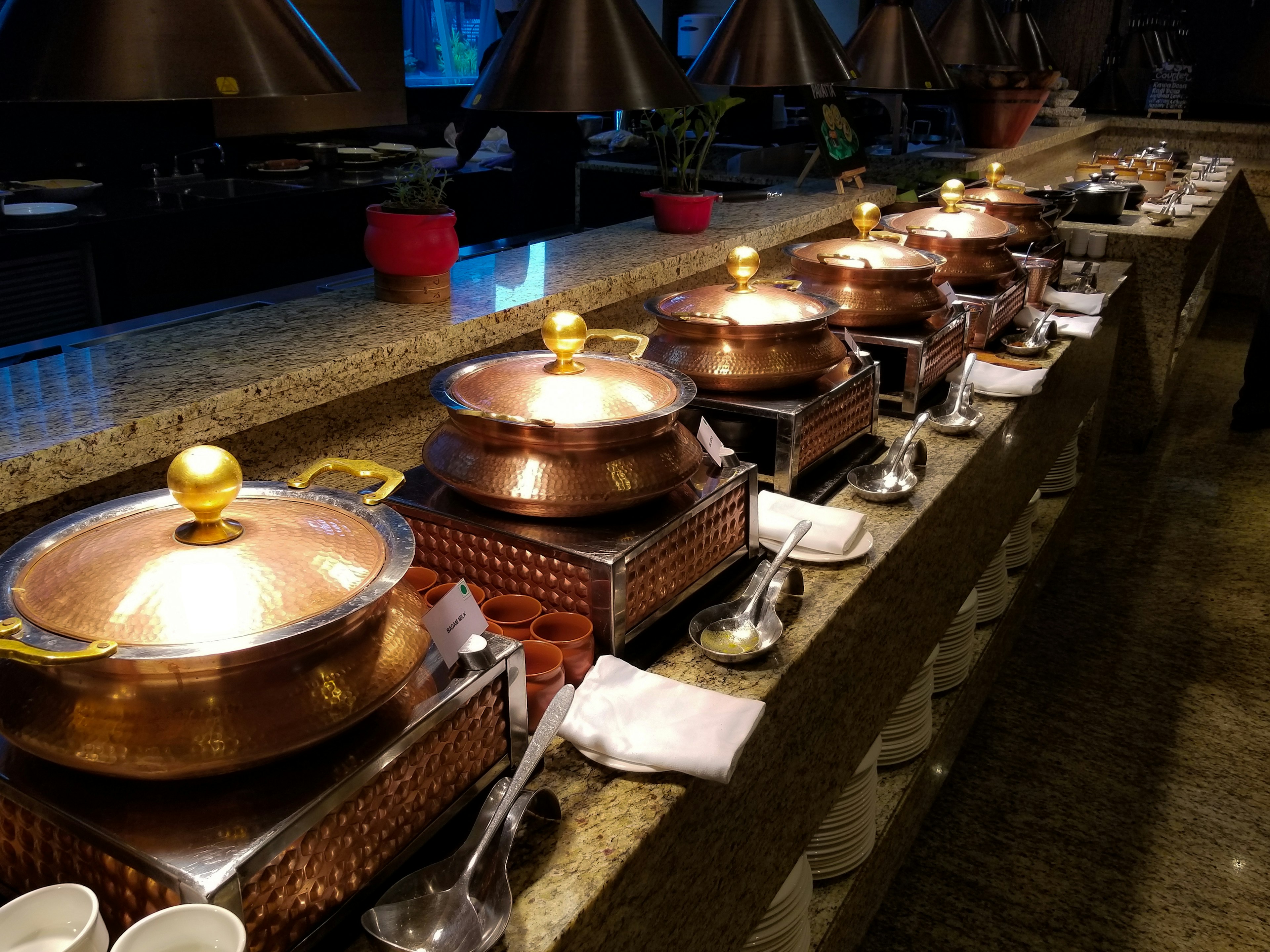 Una fila di pentole in rame su un bancone di buffet con eleganti utensili da cucina