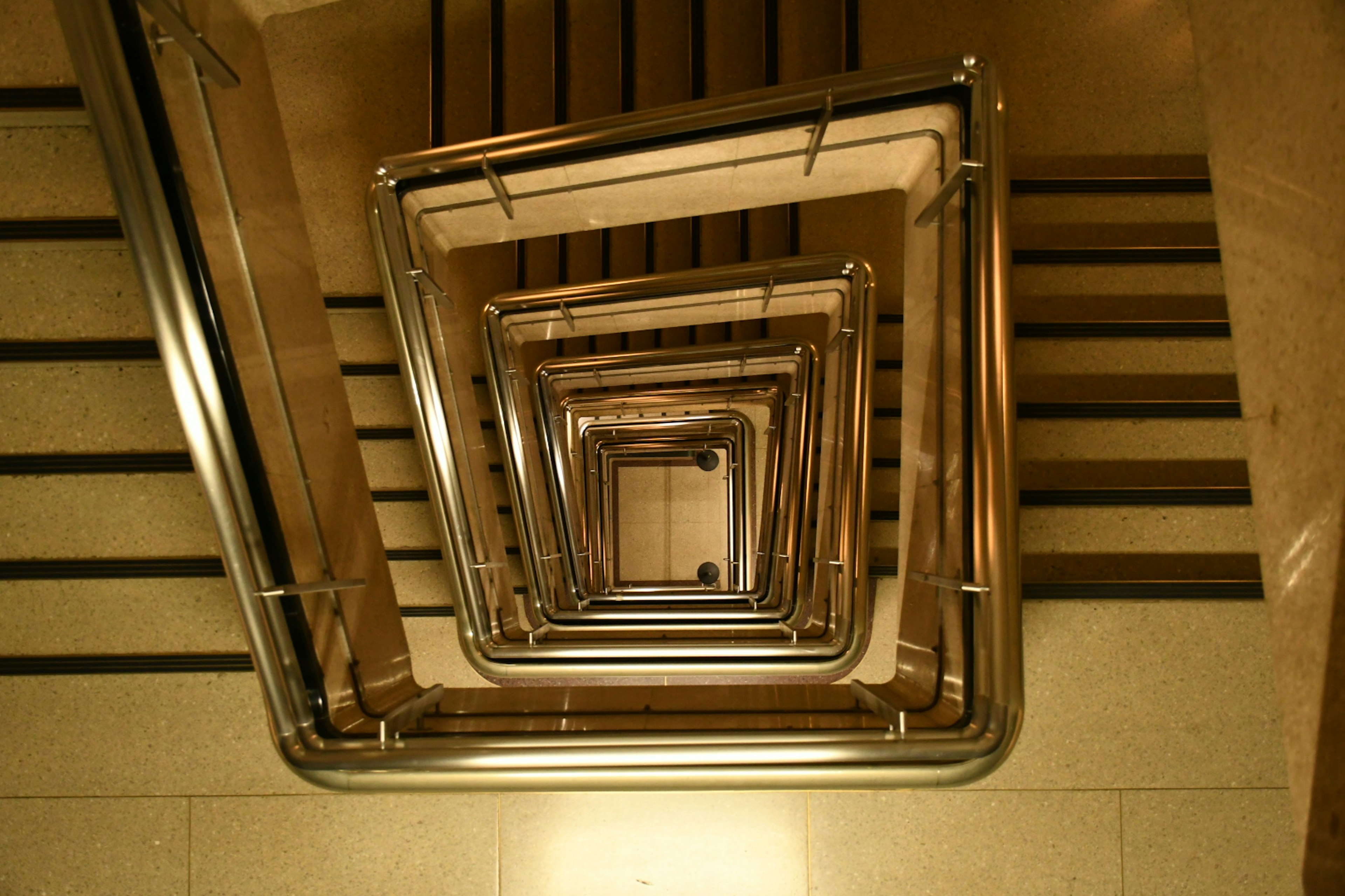 View from above of a spiral staircase with metallic railings and wooden steps