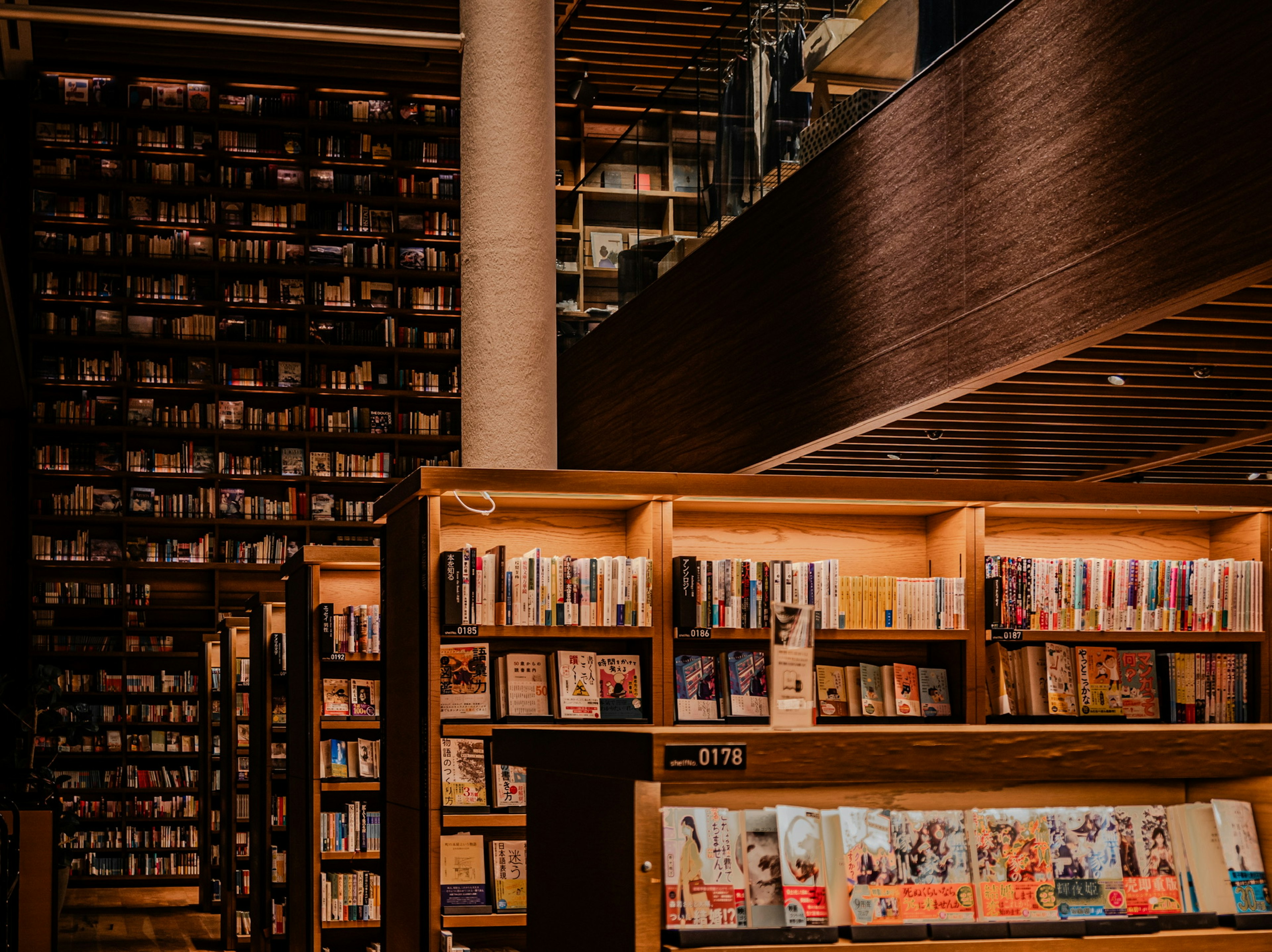 Interior perpustakaan modern dengan rak buku kayu dan buku yang ditumpuk pencahayaan hangat dan suasana nyaman