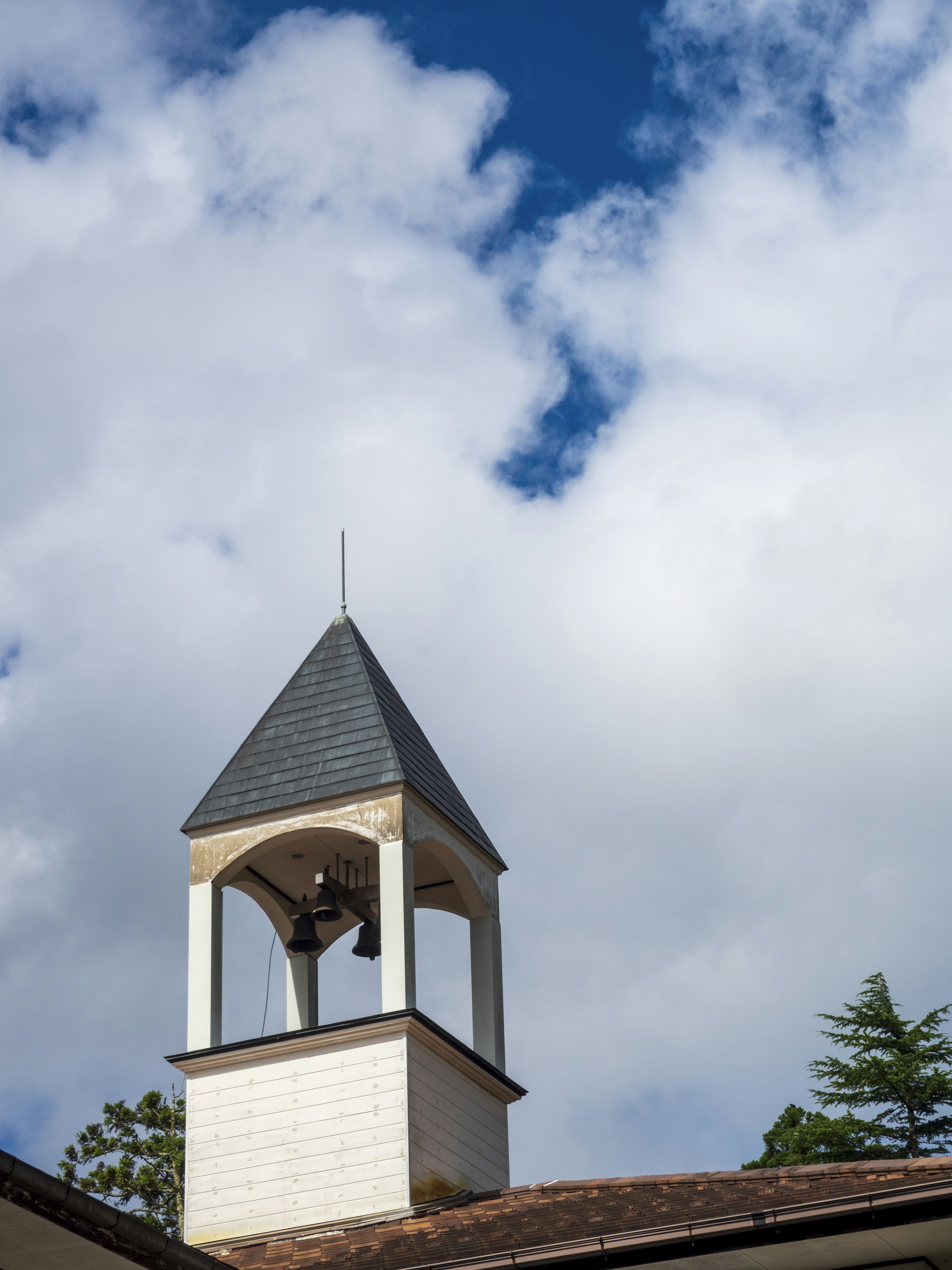 Bell tower with a slate roof against a backdrop of blue sky and white clouds