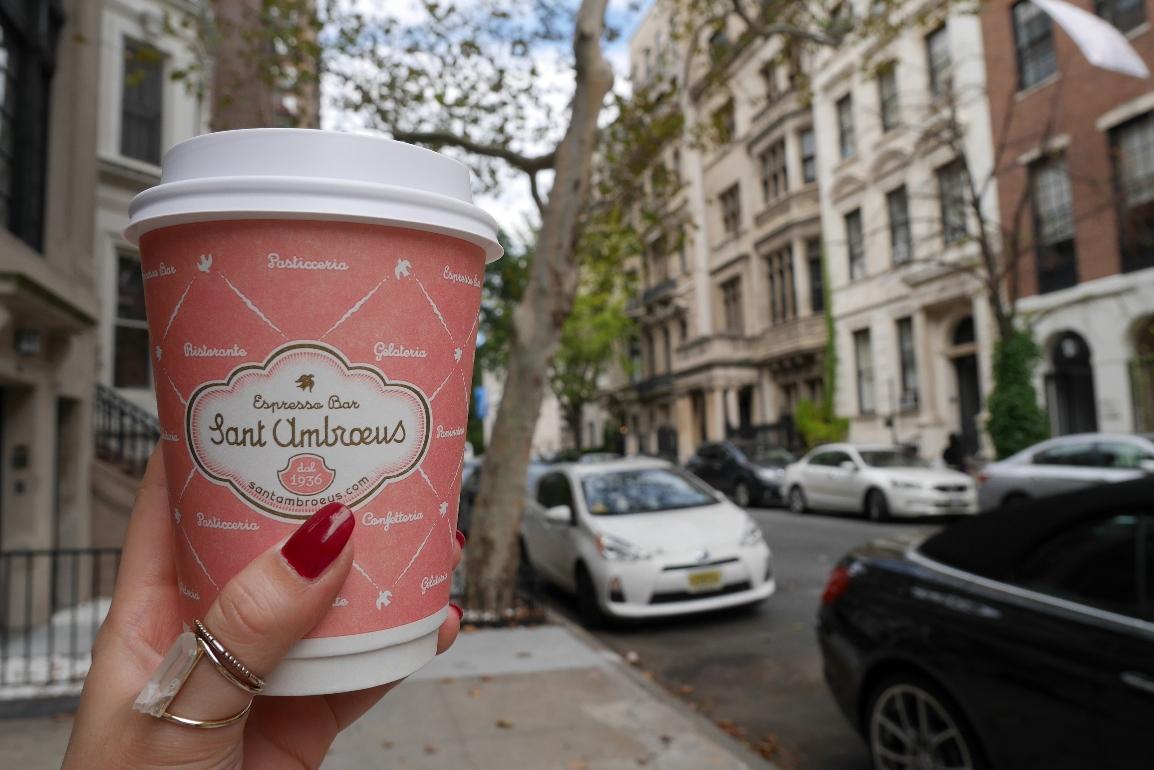 Une tasse de café rose tenue à la main avec des bâtiments en arrière-plan