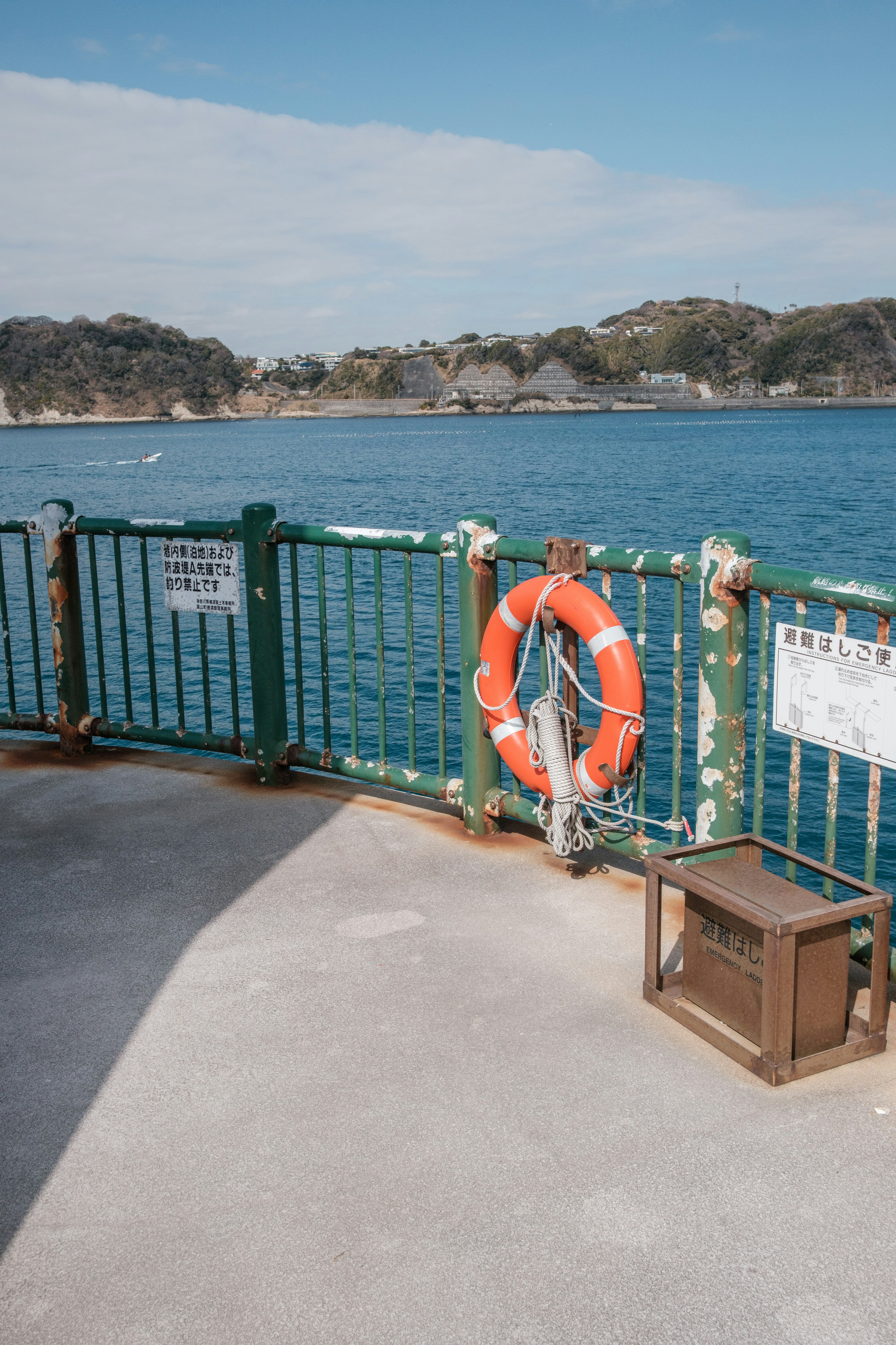 Orange life buoy hanging on a green fence near the sea with visible landscape