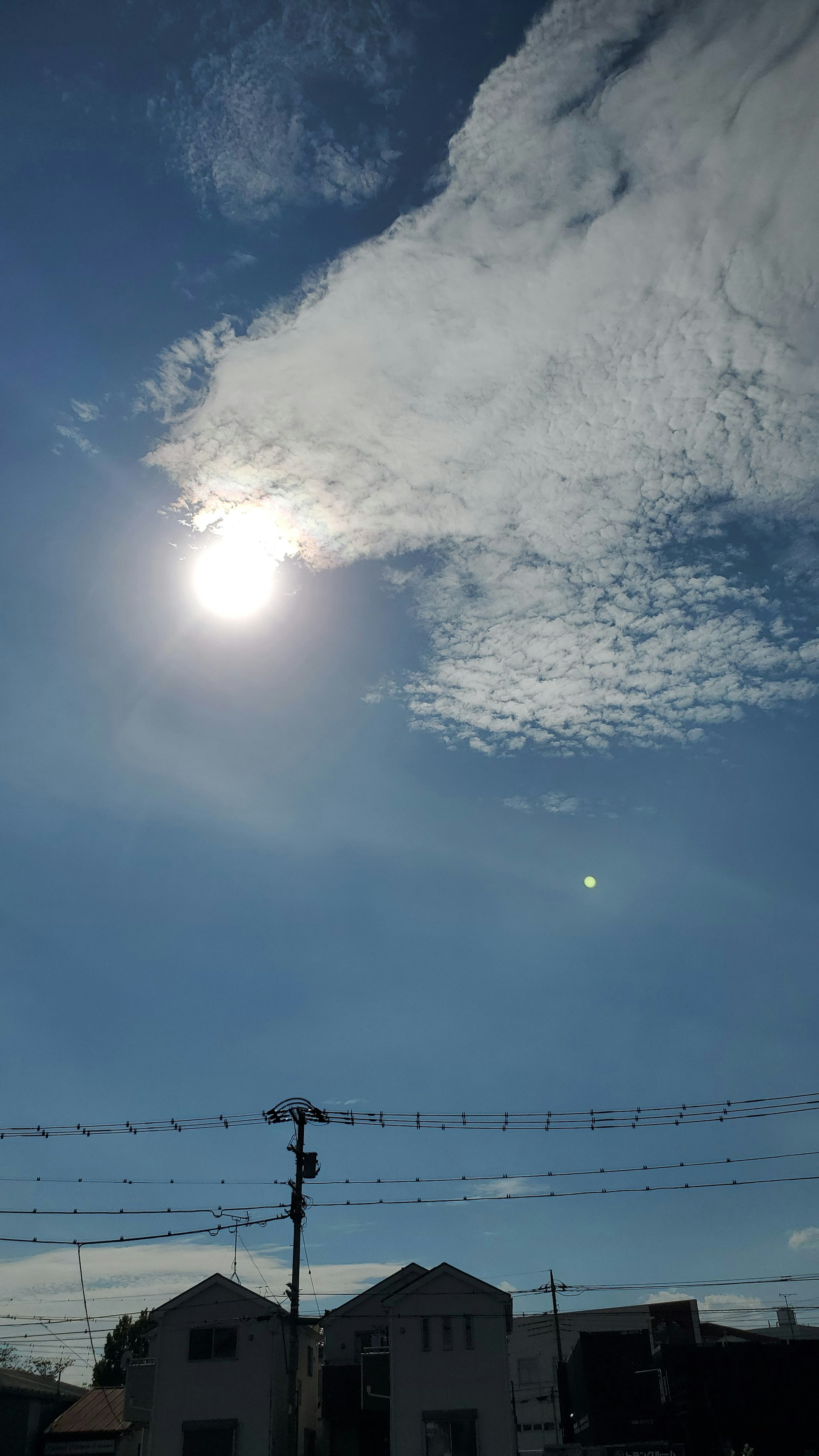 Bright sun shining in a blue sky with white clouds and houses below