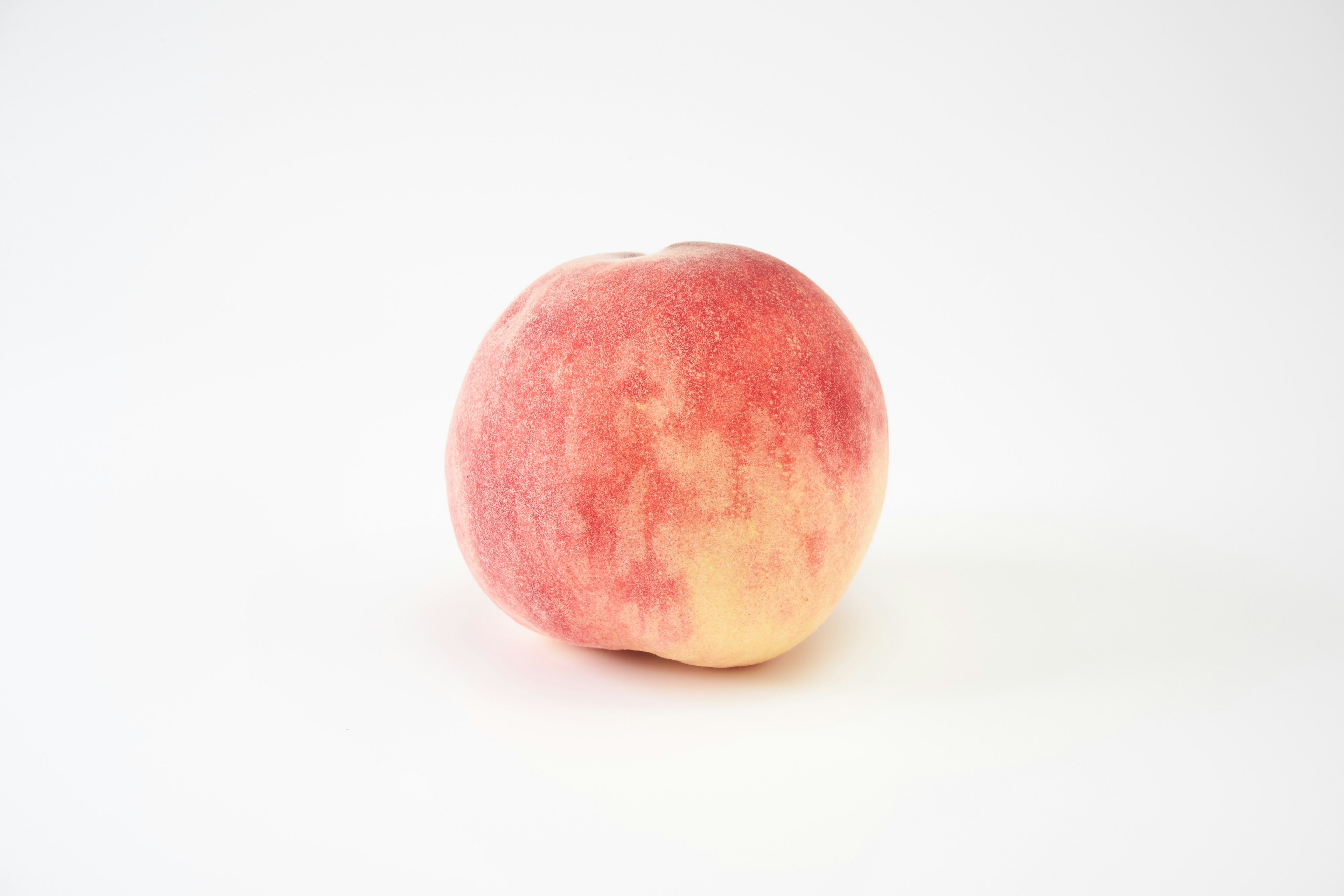 A vibrant red and yellow peach placed on a white background