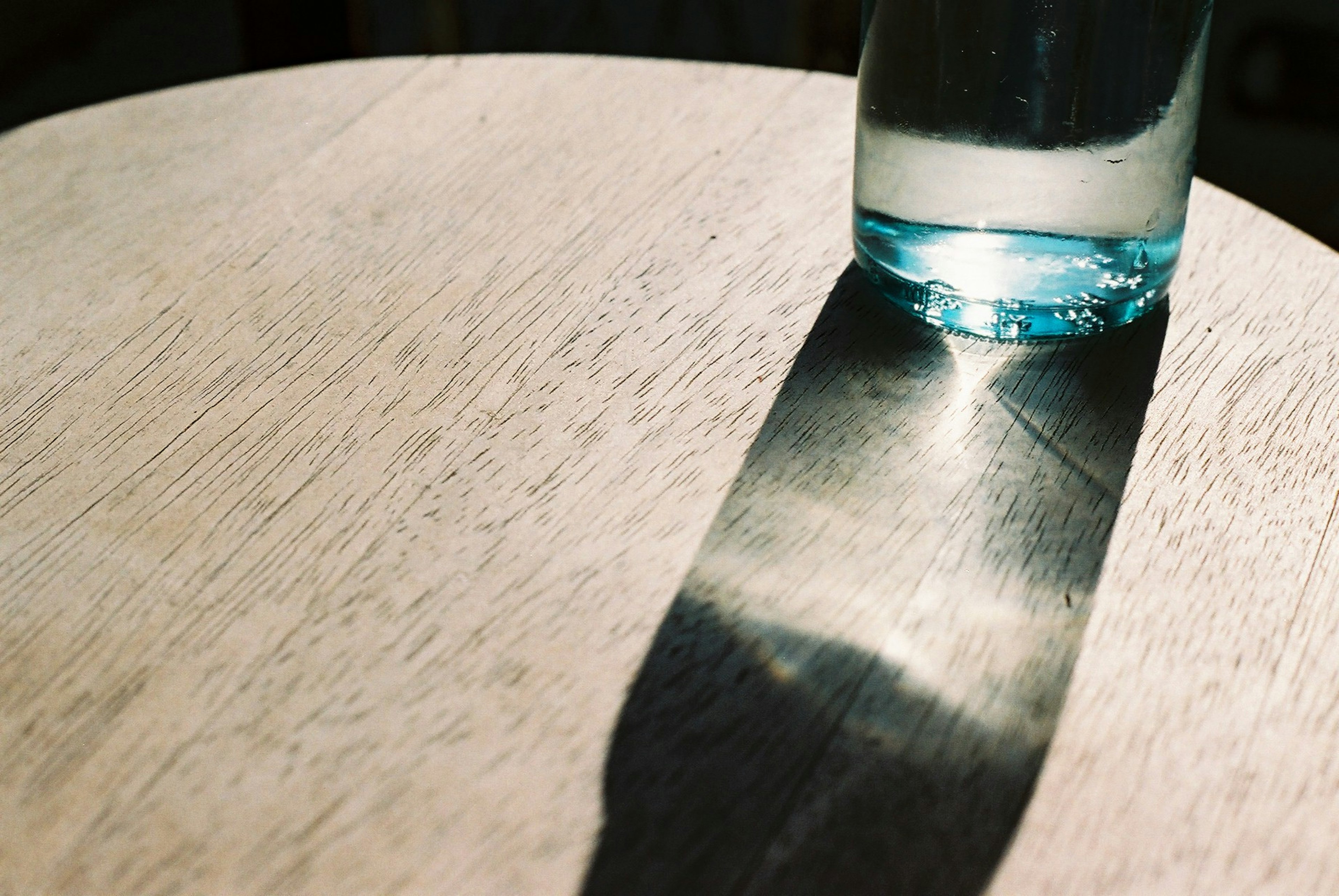 A glass of water casting a shadow on a wooden table