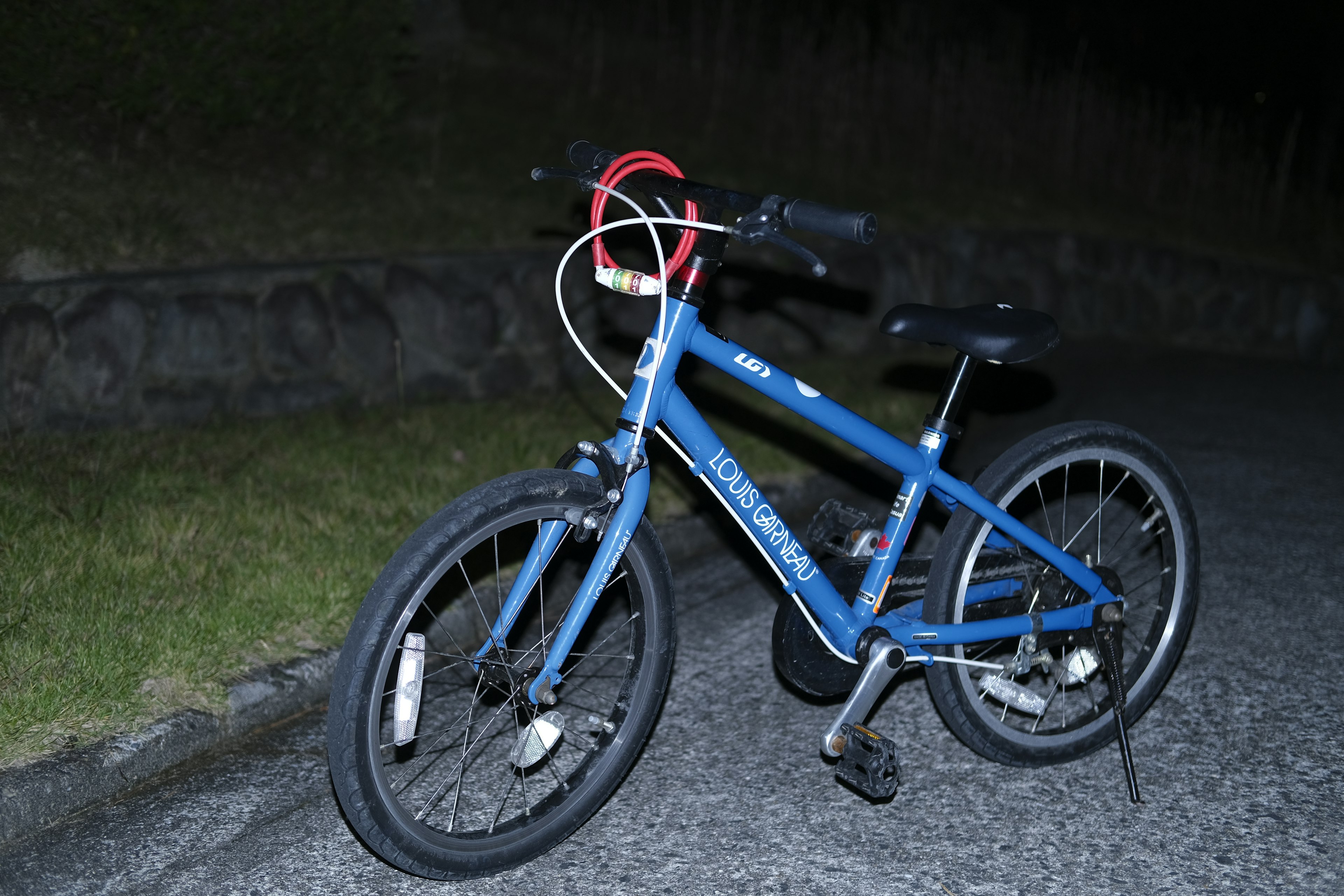 A blue bicycle parked on a nighttime road featuring silver wheels and a red handlebar