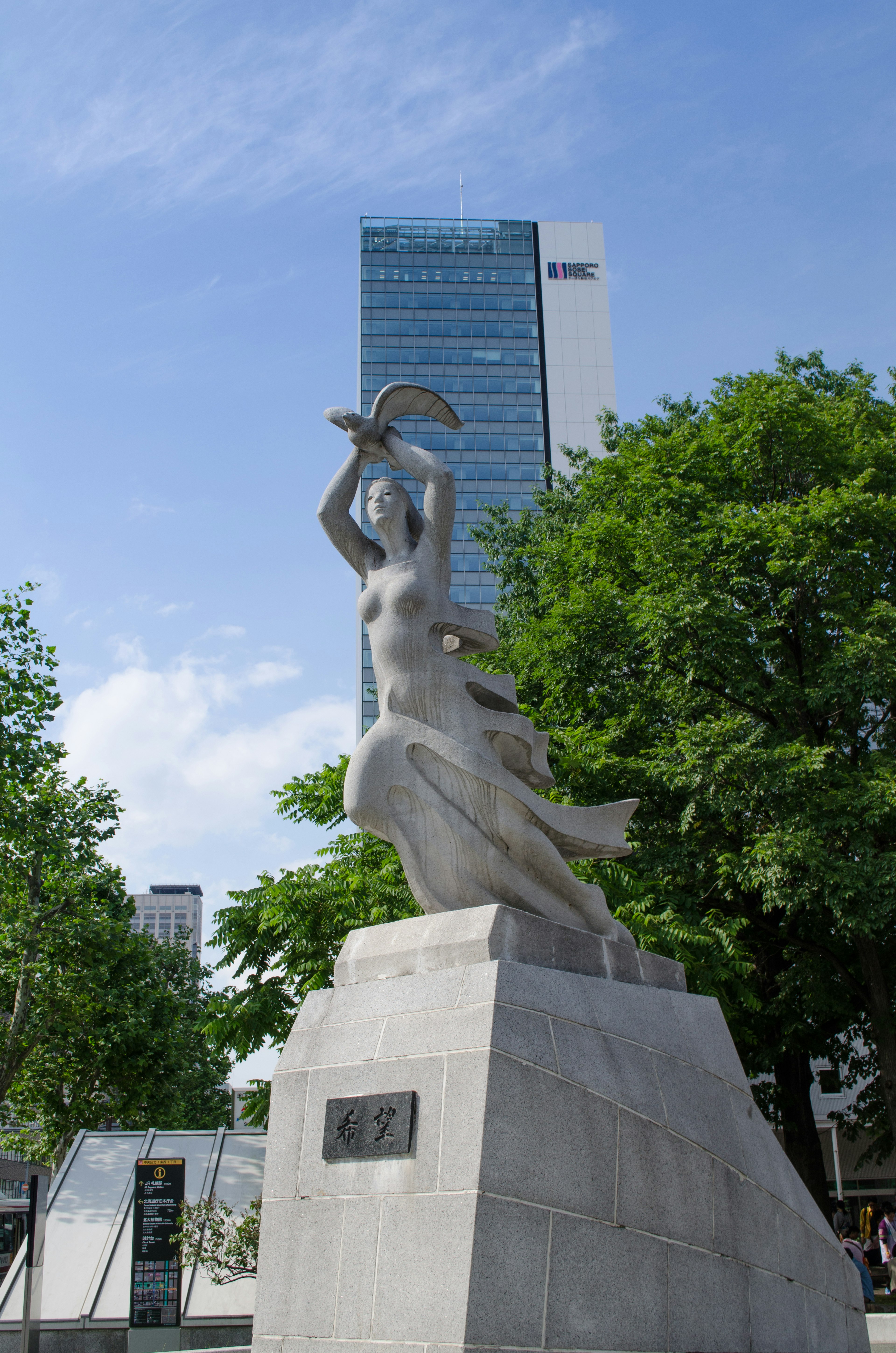 Sculpture of a woman holding a bird with a skyscraper in the background