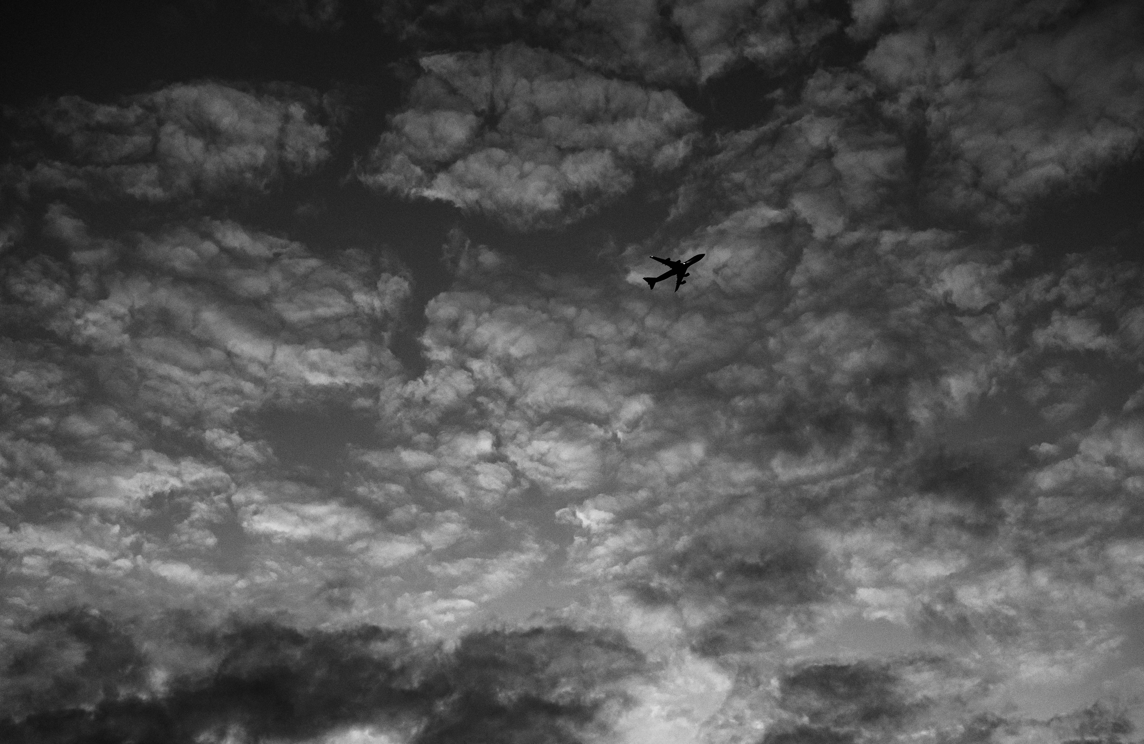 Schwarzweißbild eines Flugzeugs, das durch einen bewölkten Himmel fliegt