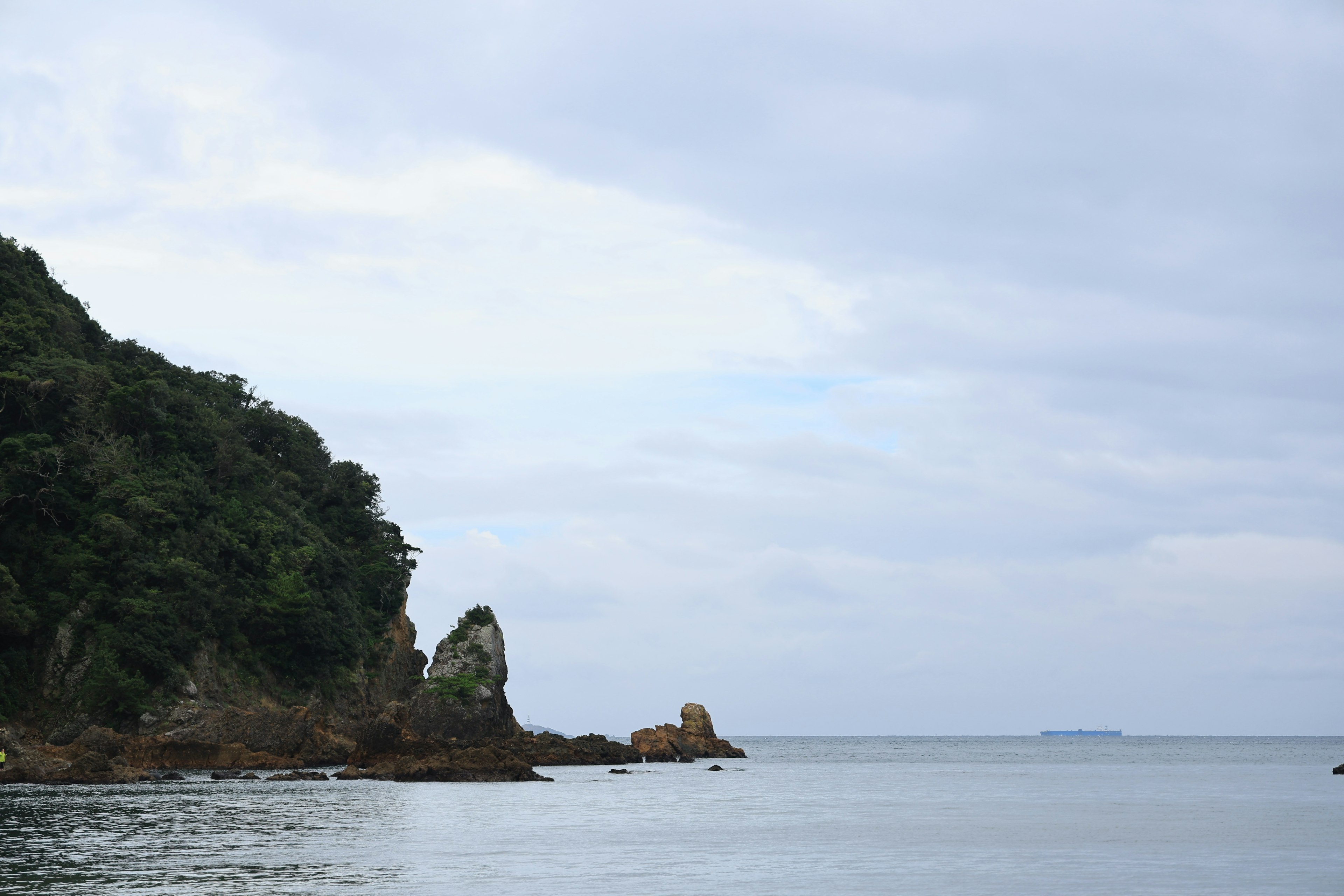 Malersicher Blick auf ein ruhiges Meer mit einer felsigen Klippe und bewölktem Himmel