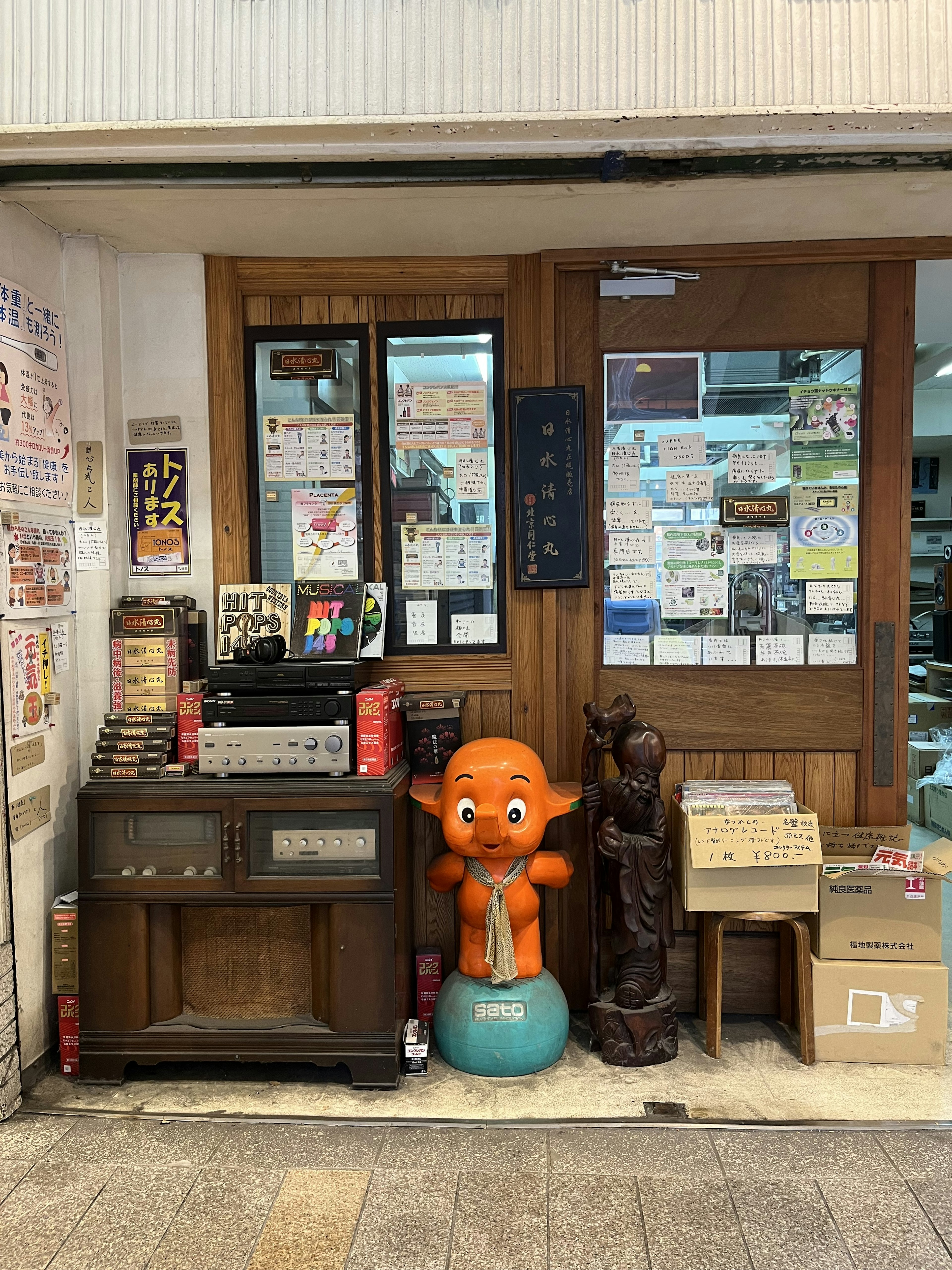 Entrada de una tienda con una estatua de personaje naranja y una escultura de madera rodeadas de postales