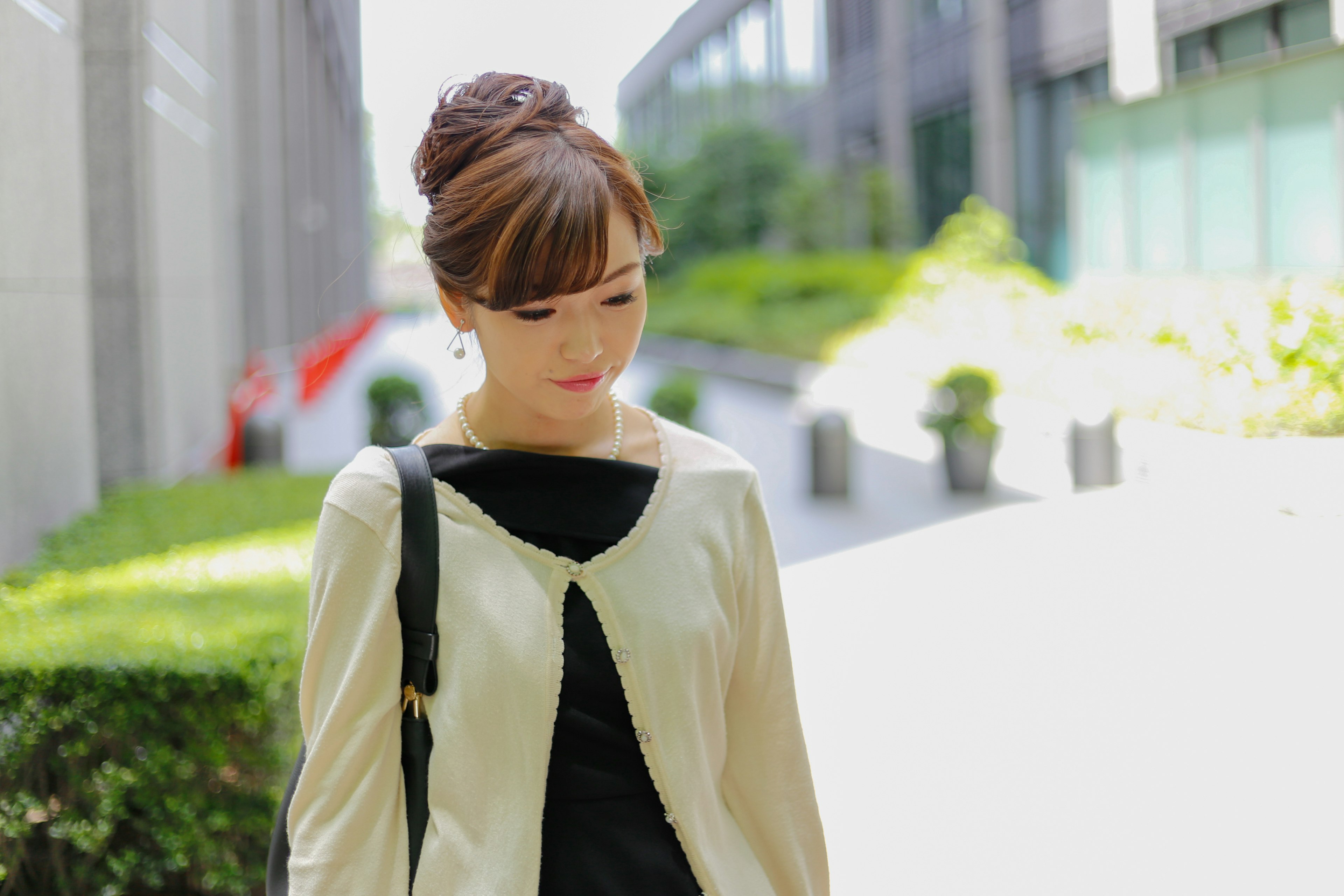 A woman walking in front of an office building wearing a white jacket and black top with her hair styled up