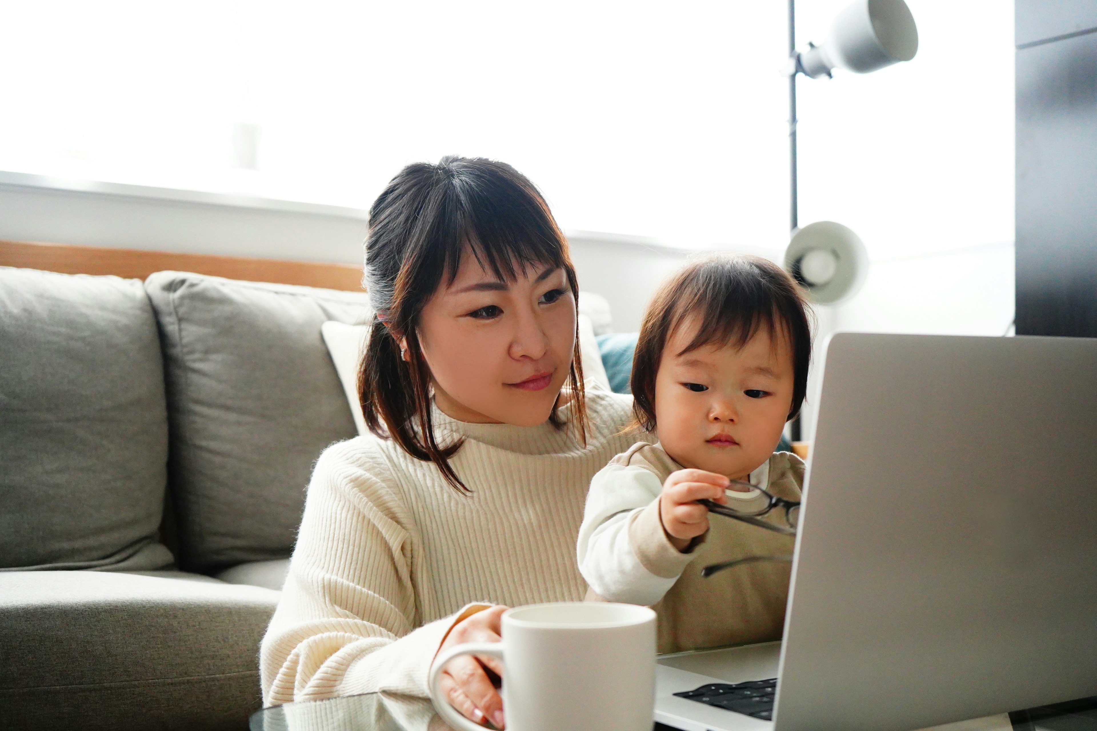 Una madre usando una computadora portátil con su hijo al lado