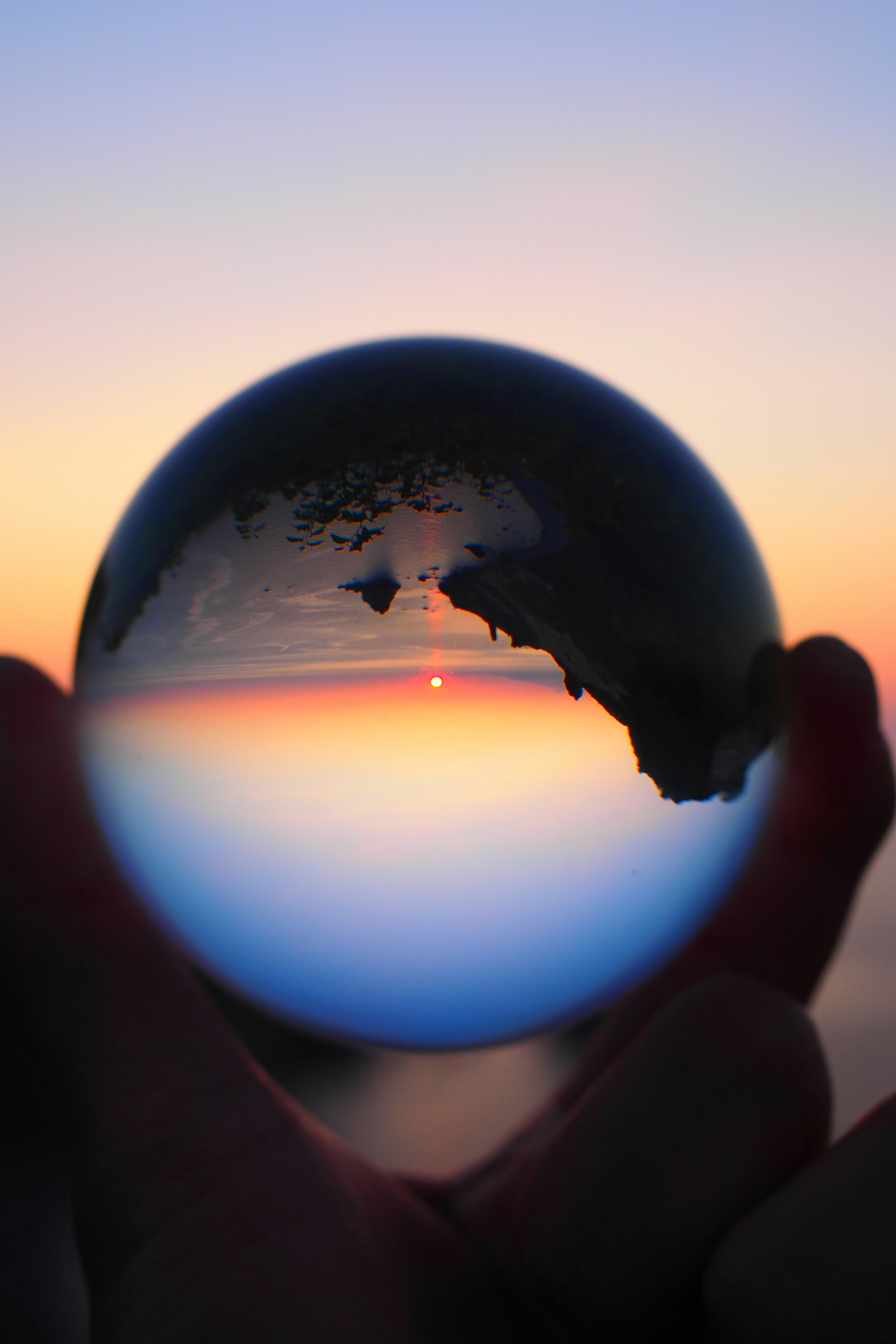 Silhouette di una mano che tiene una sfera di cristallo che riflette un tramonto