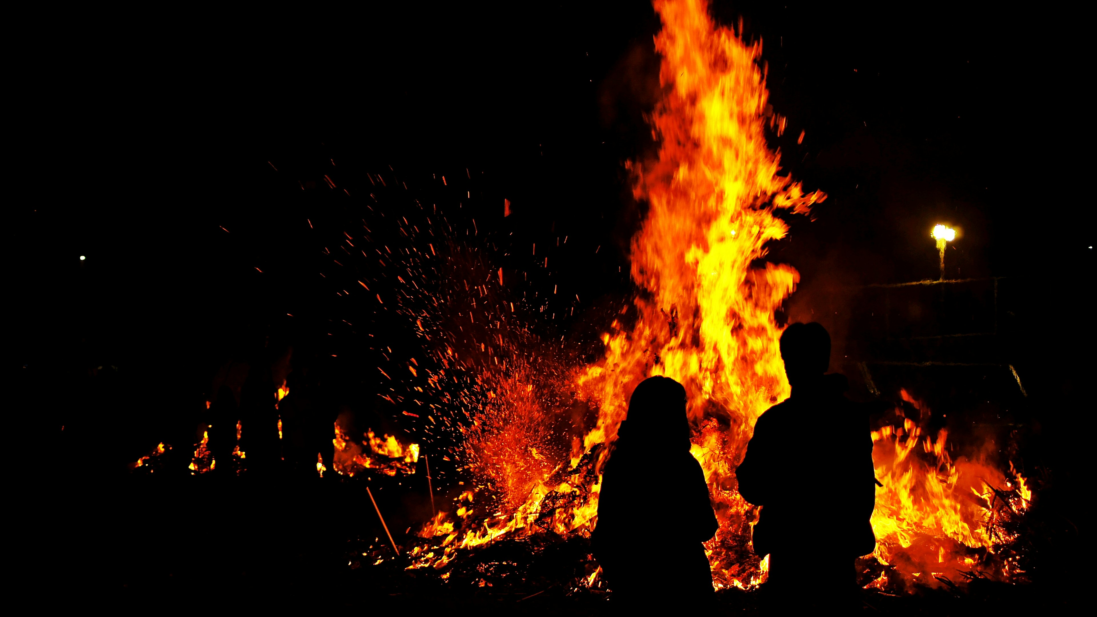 Silhouettes of people standing in front of a bonfire at night