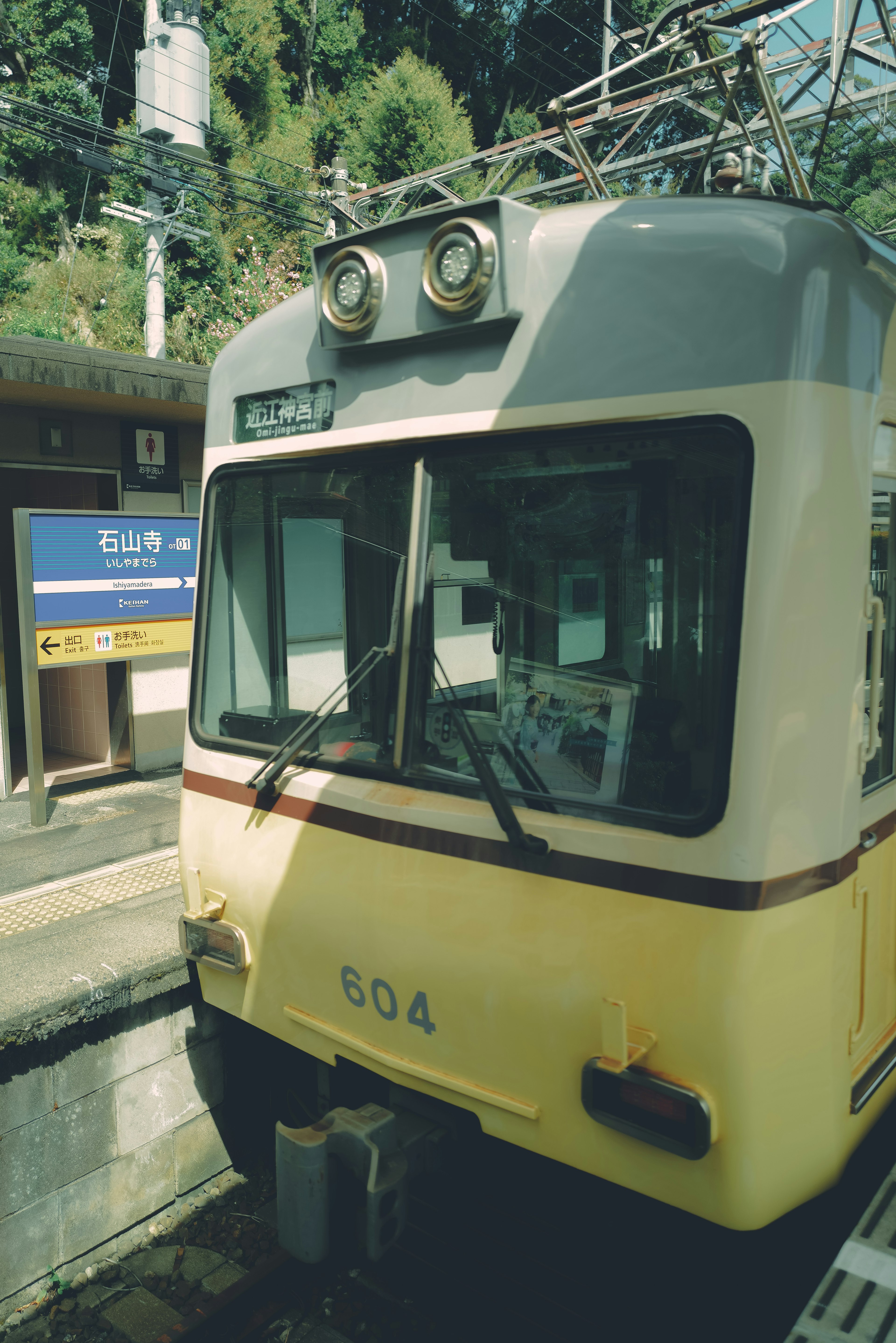 มุมมองด้านหน้าของรถไฟสีเหลืองที่สถานีพร้อมภูเขาสีเขียวด้านหลัง