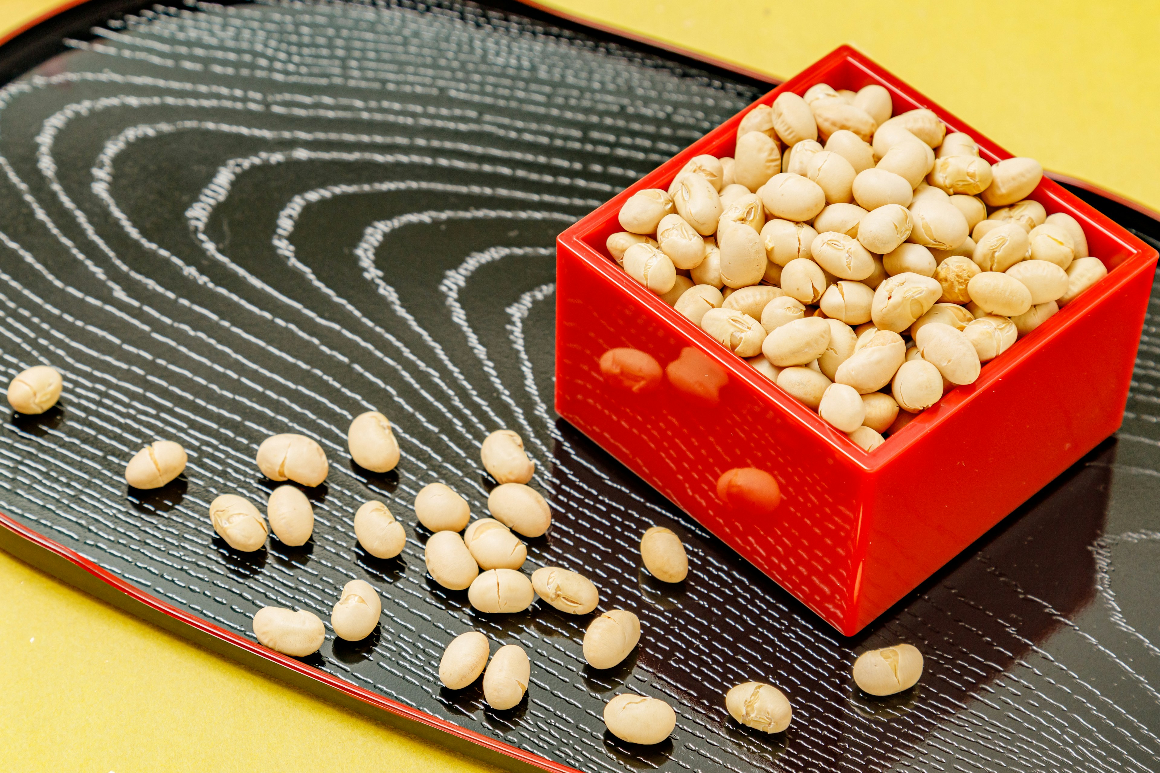 Frijoles blancos en una caja roja sobre un plato negro con fondo amarillo