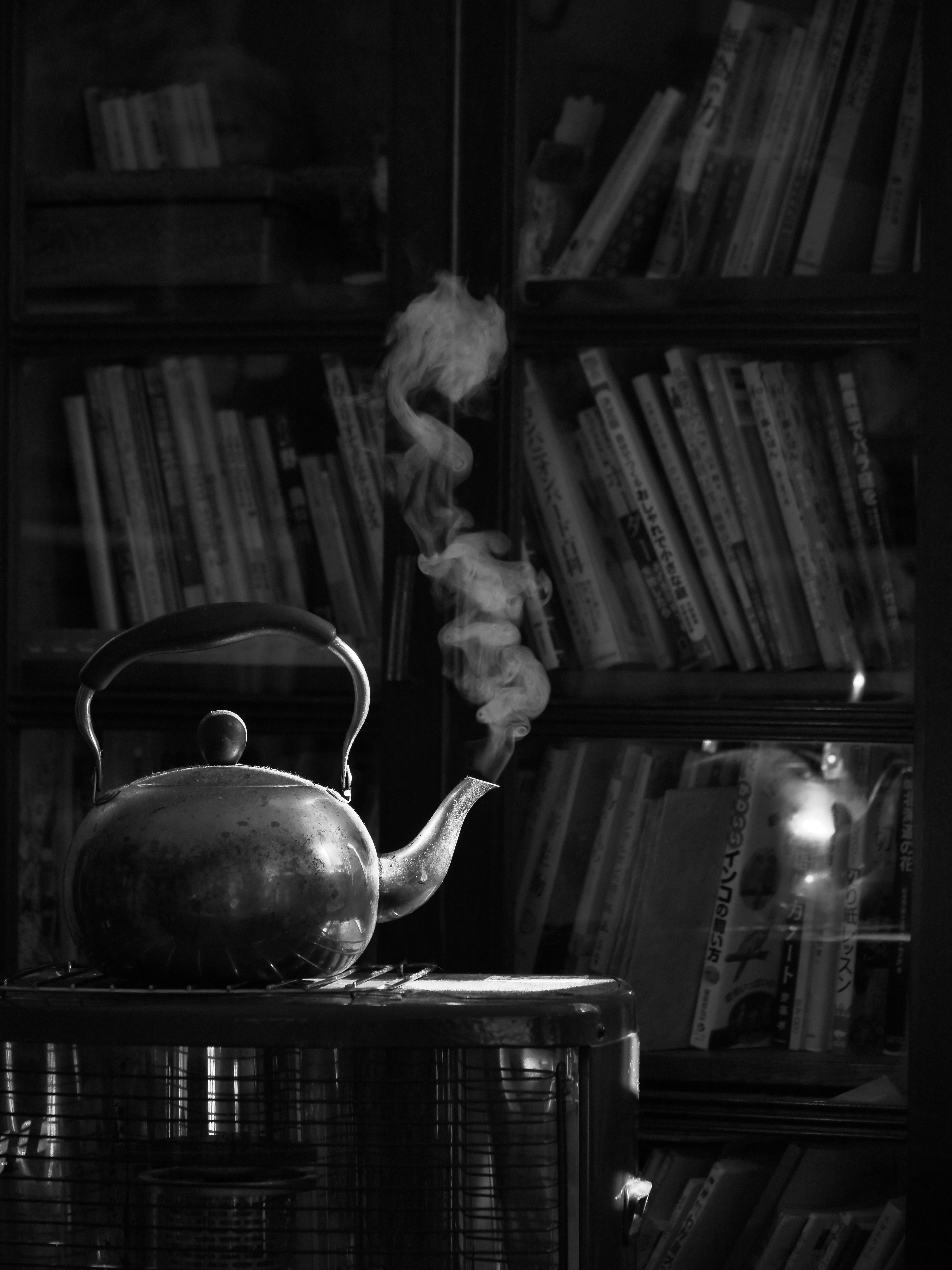 Image en noir et blanc d'une bouilloire fumante sur une table avec une bibliothèque en arrière-plan