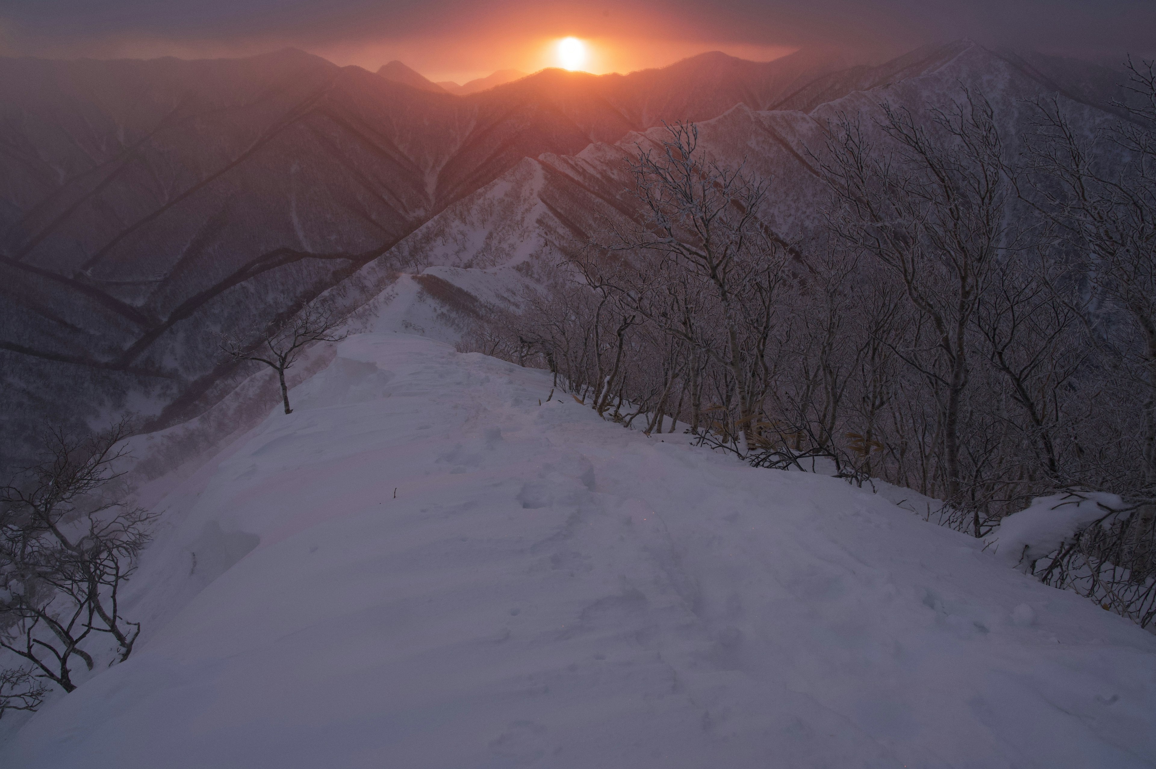 雪に覆われた山脈の上に昇る夕日