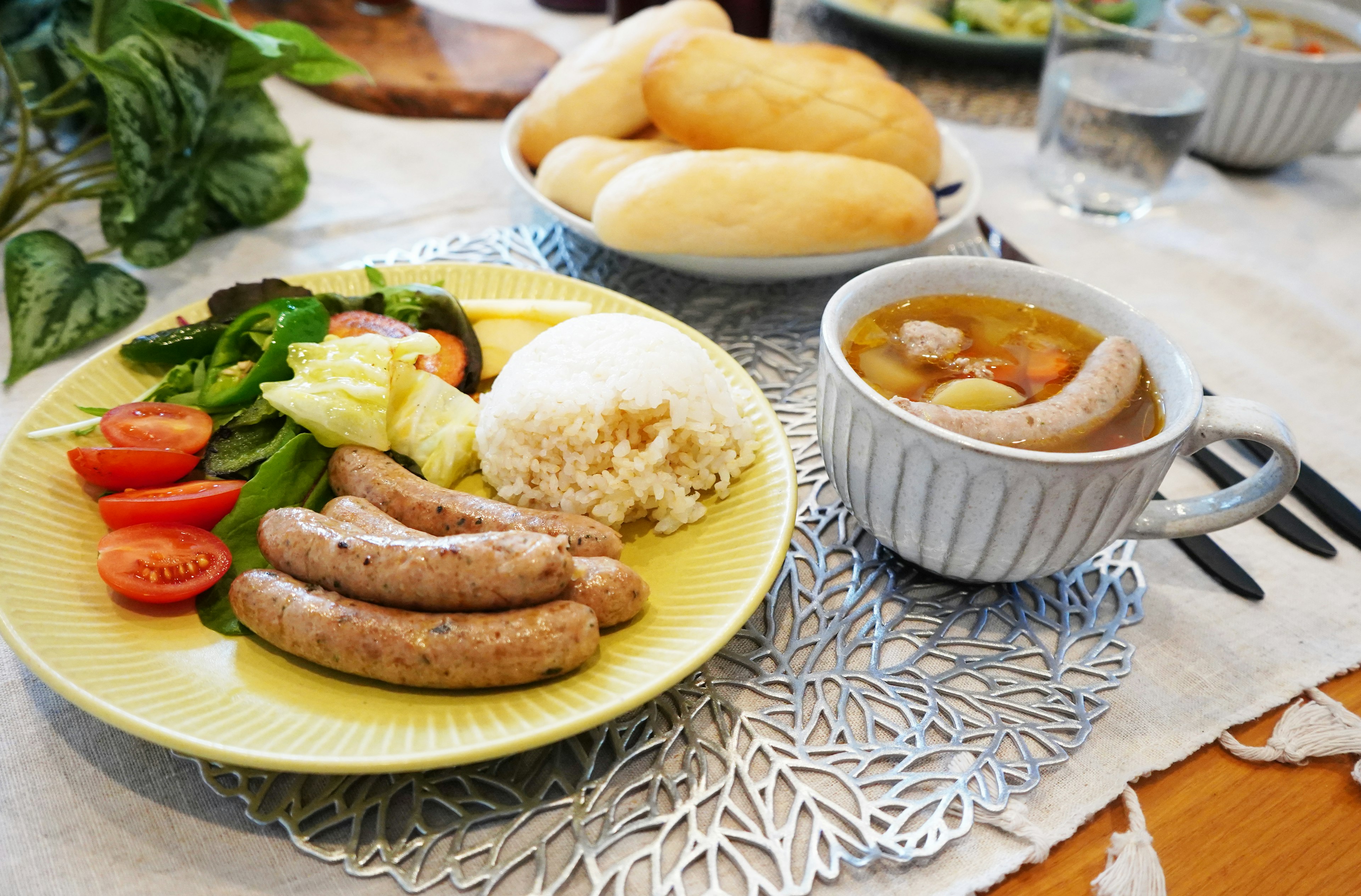 Une assiette avec des saucisses, une salade, du riz et un bol de soupe sur une table à manger