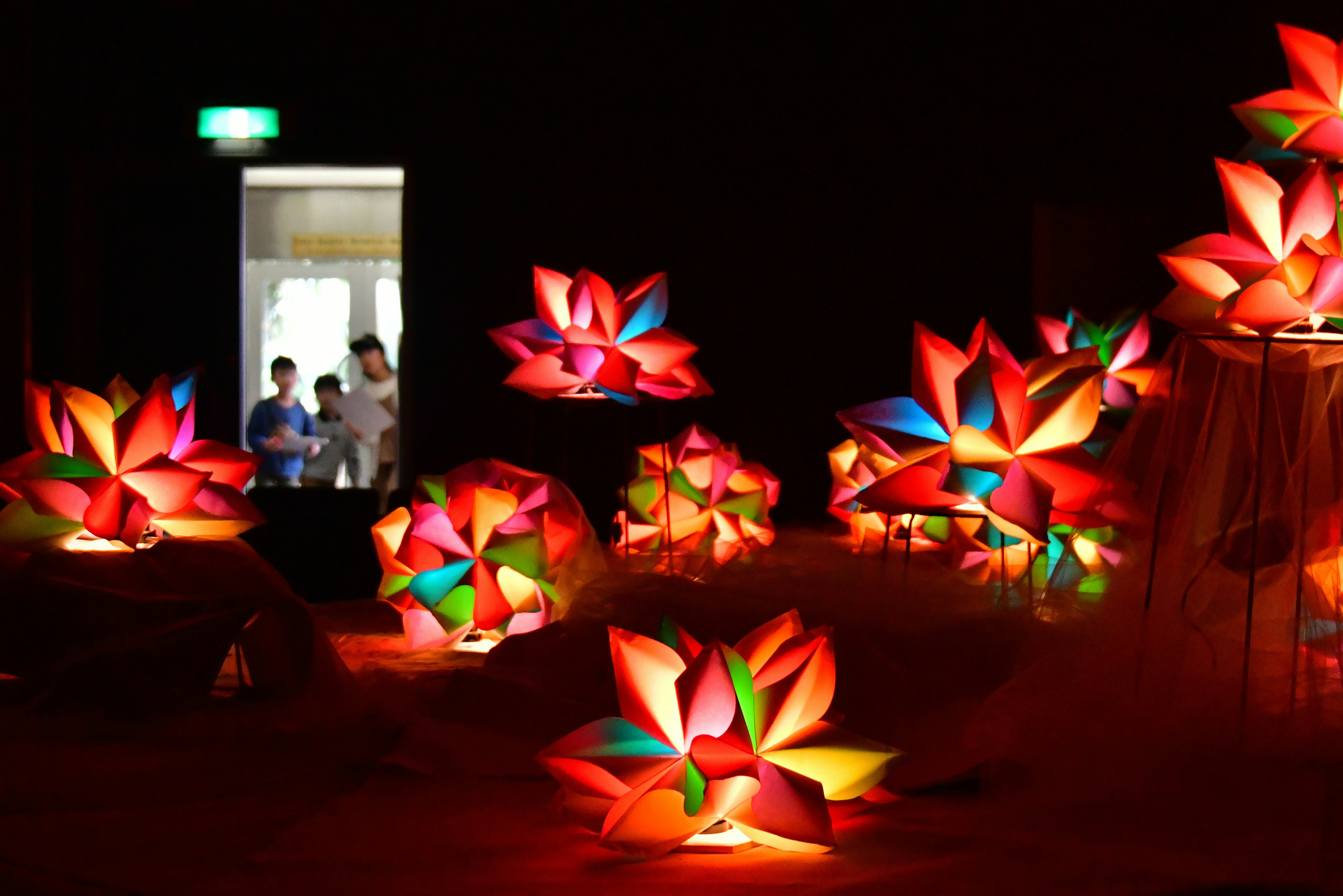 色とりどりの花の形をしたランプが並ぶ暗い空間の中に人々が見える