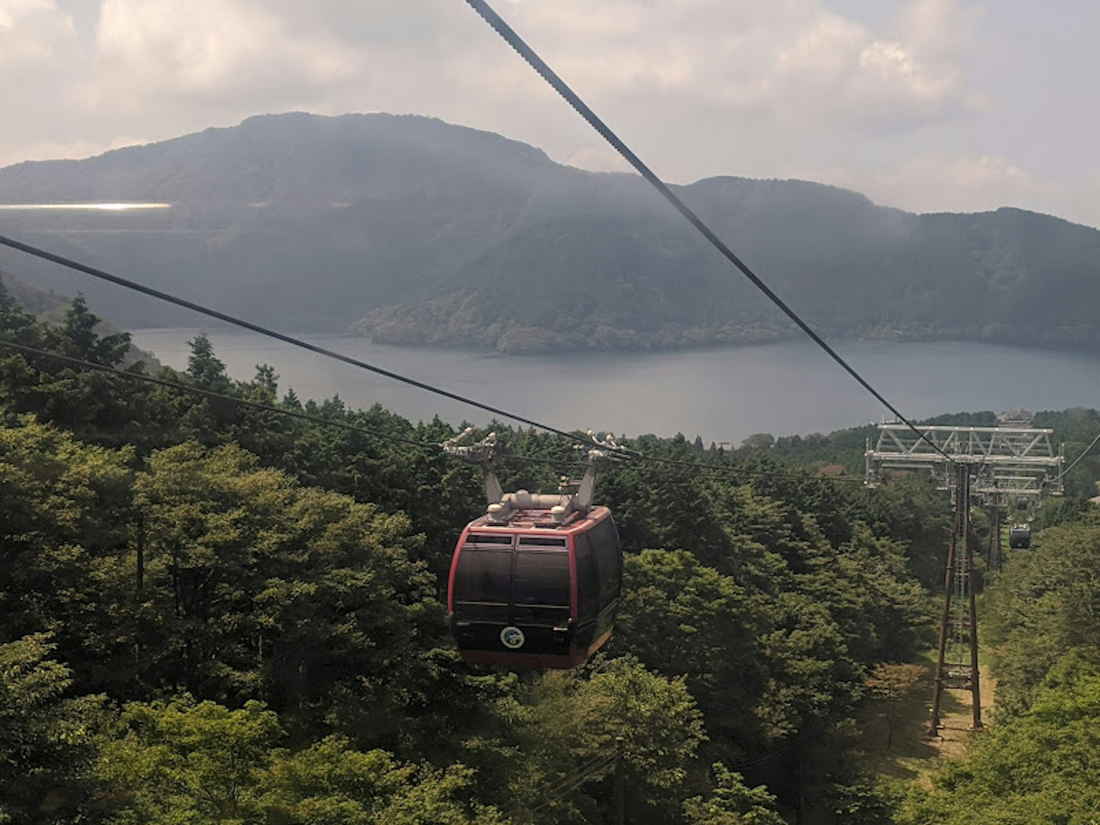 Red gondola moving above green mountains with a lake in the background