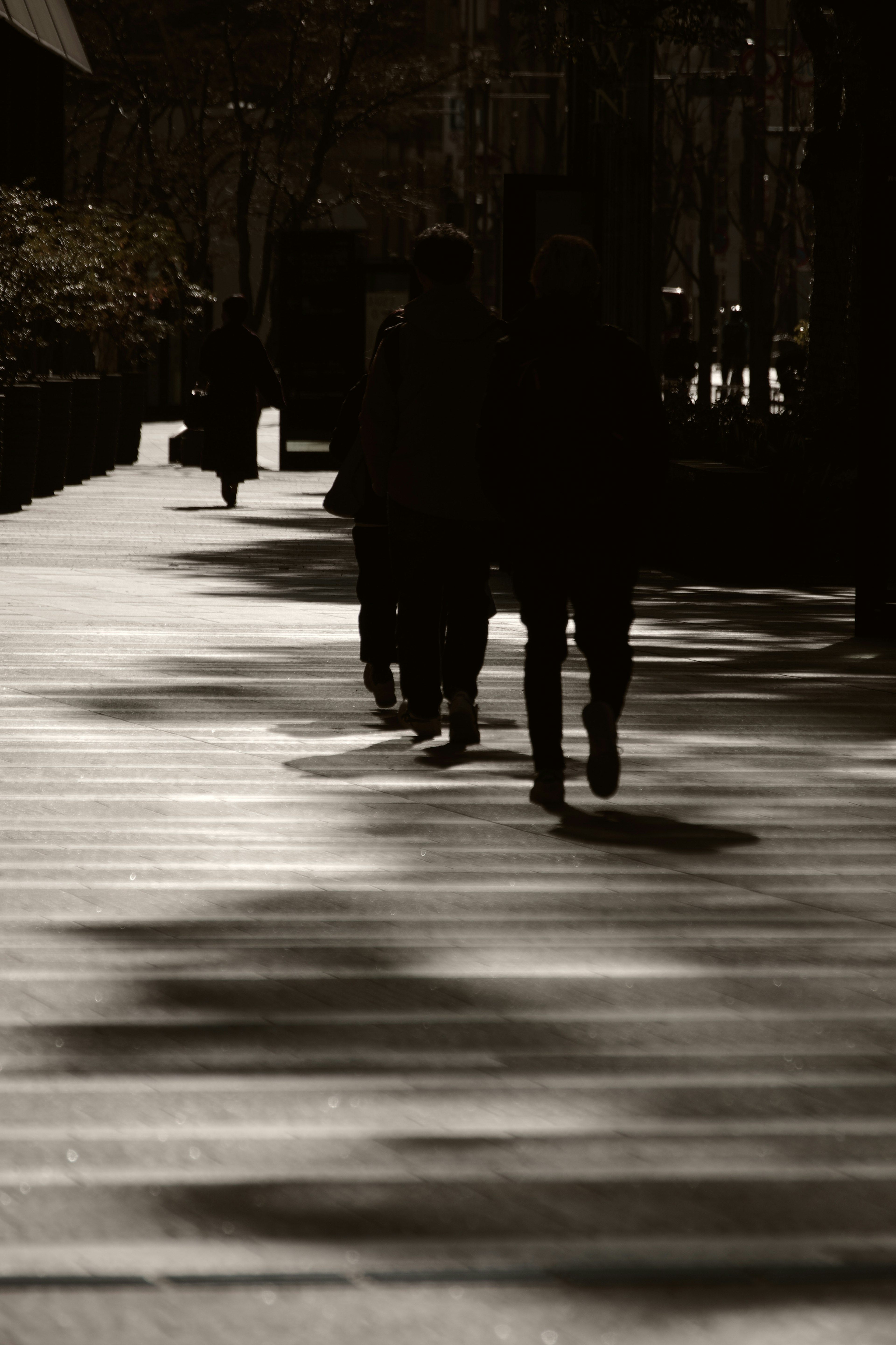 Figure in silhouette che camminano su un marciapiede ombreggiato