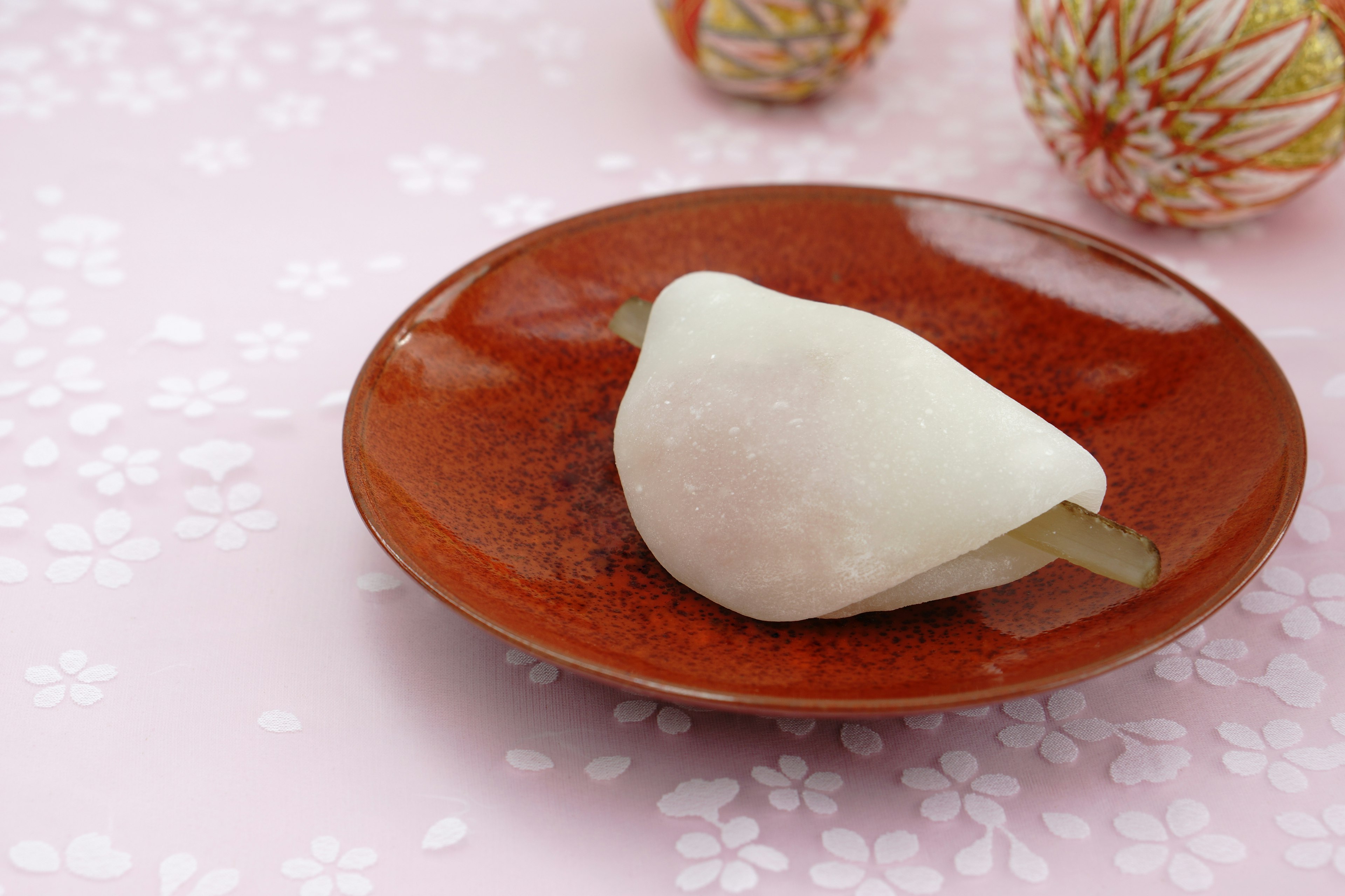 A white Japanese sweet on a red plate with scattered cherry blossom petals in the background