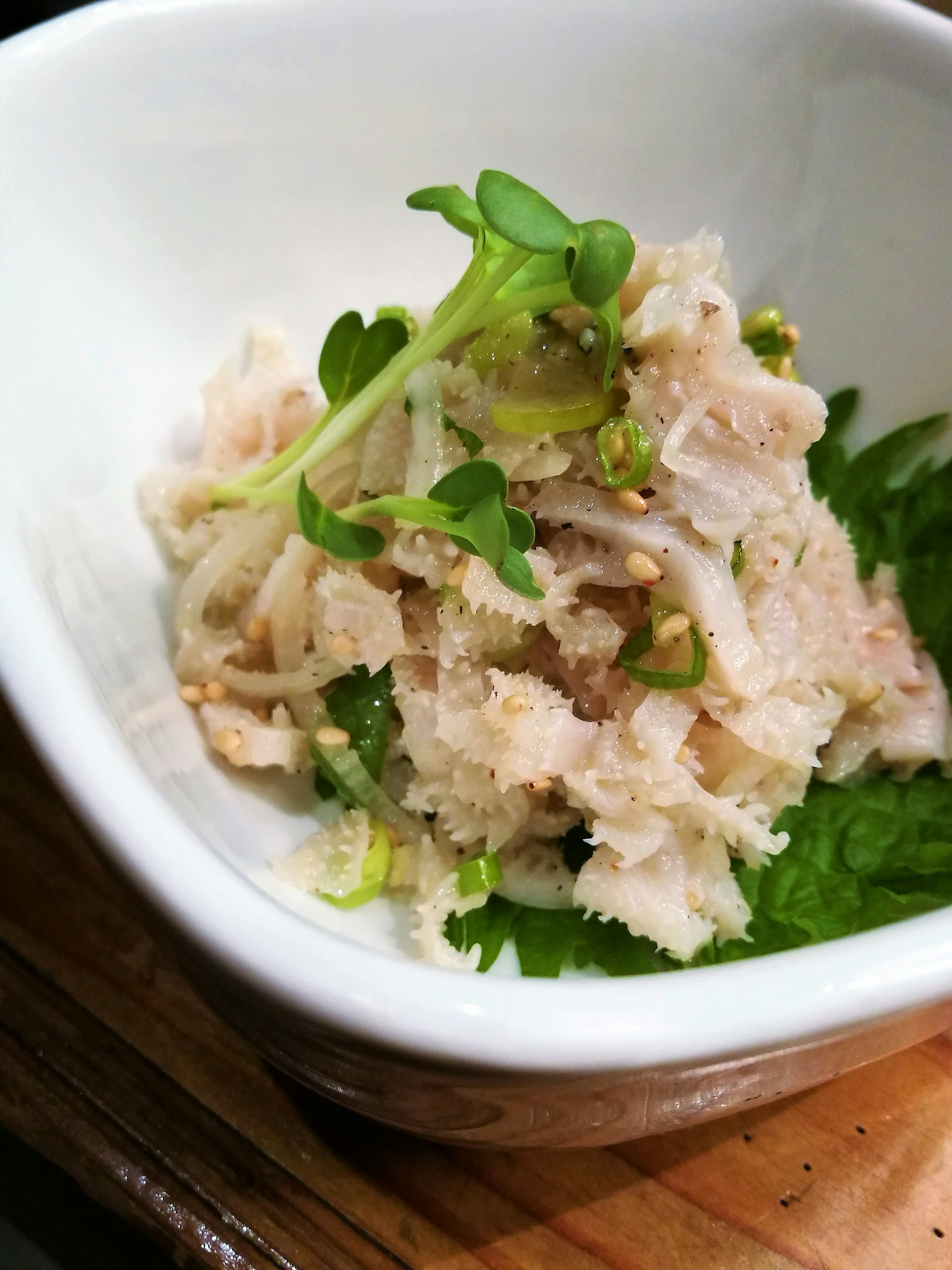 Hühnchensalat in einer weißen Schüssel mit frischen Kräutern und Sesamsamen serviert