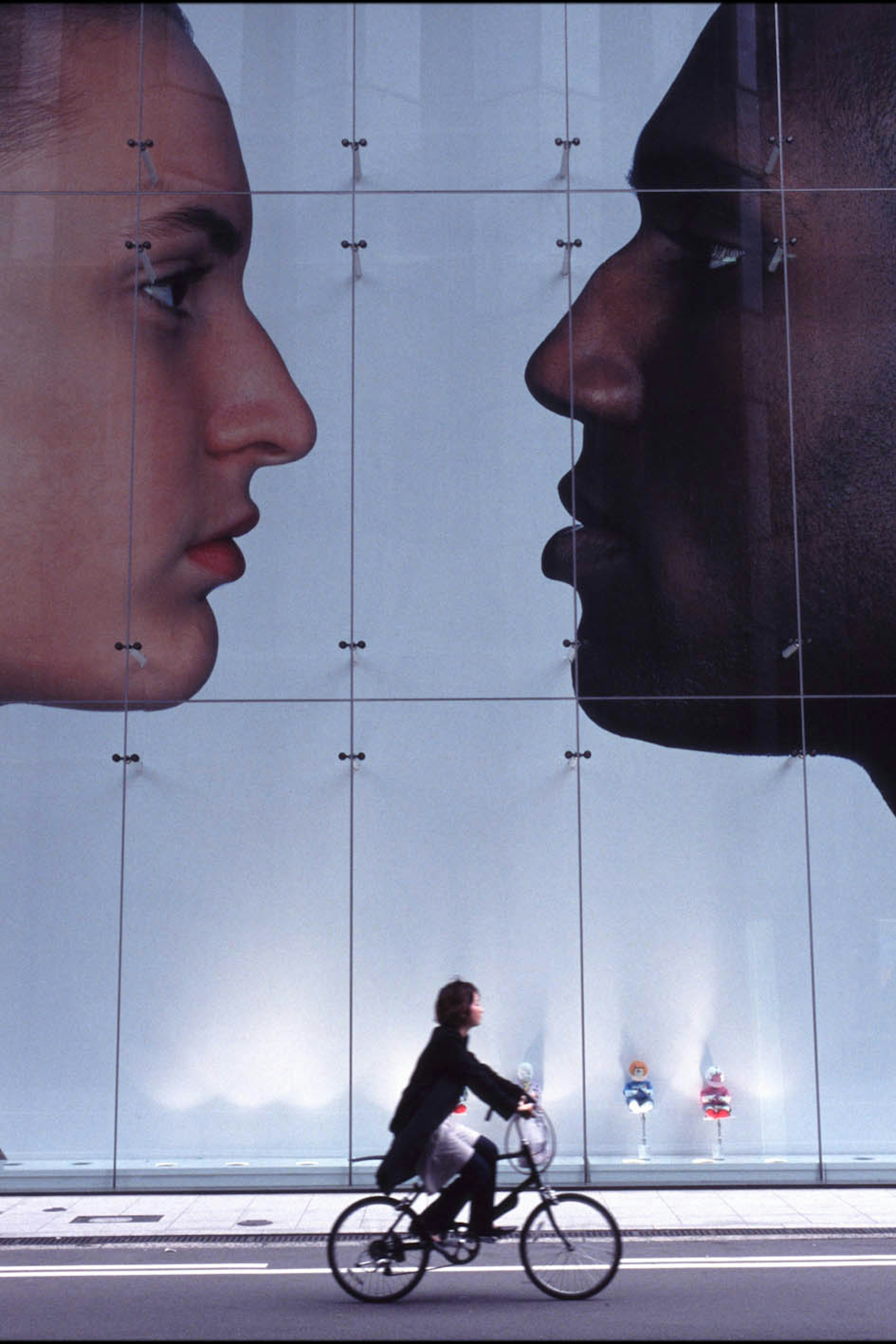 A cyclist passing in front of a large mural depicting two faces