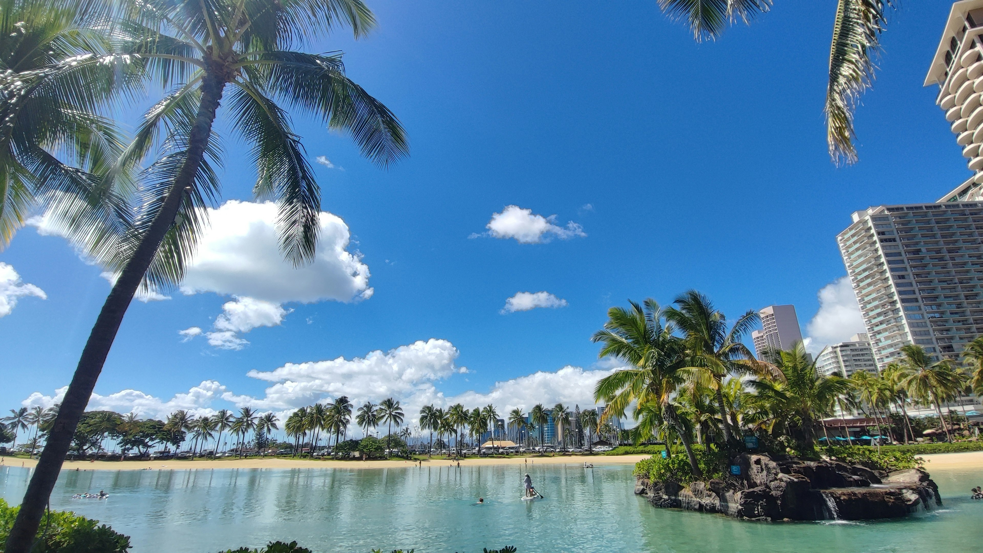 Beach scene with blue sky and white clouds featuring palm trees and turquoise water