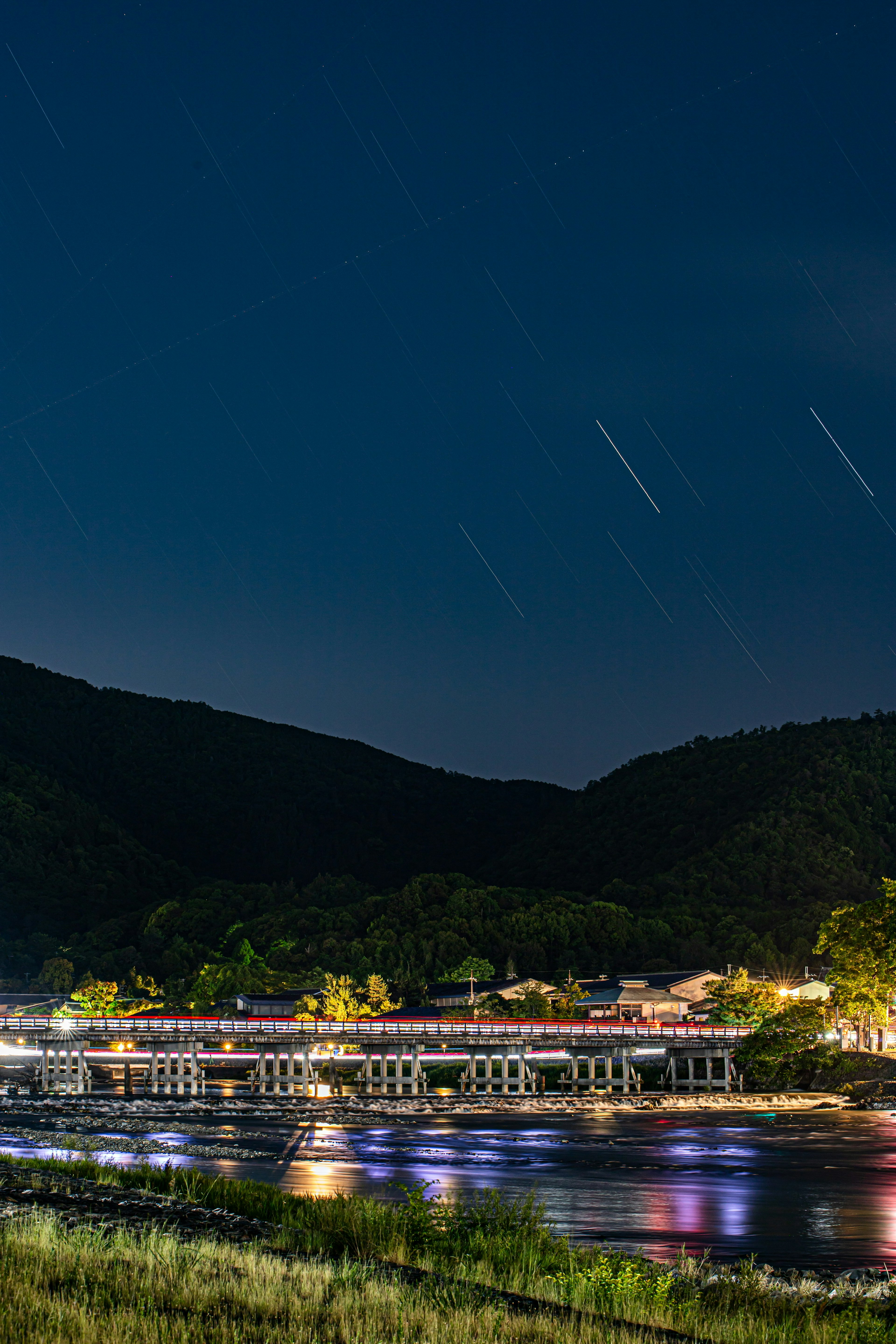 Escena nocturna de un río con rastros de estrellas y un puente iluminado