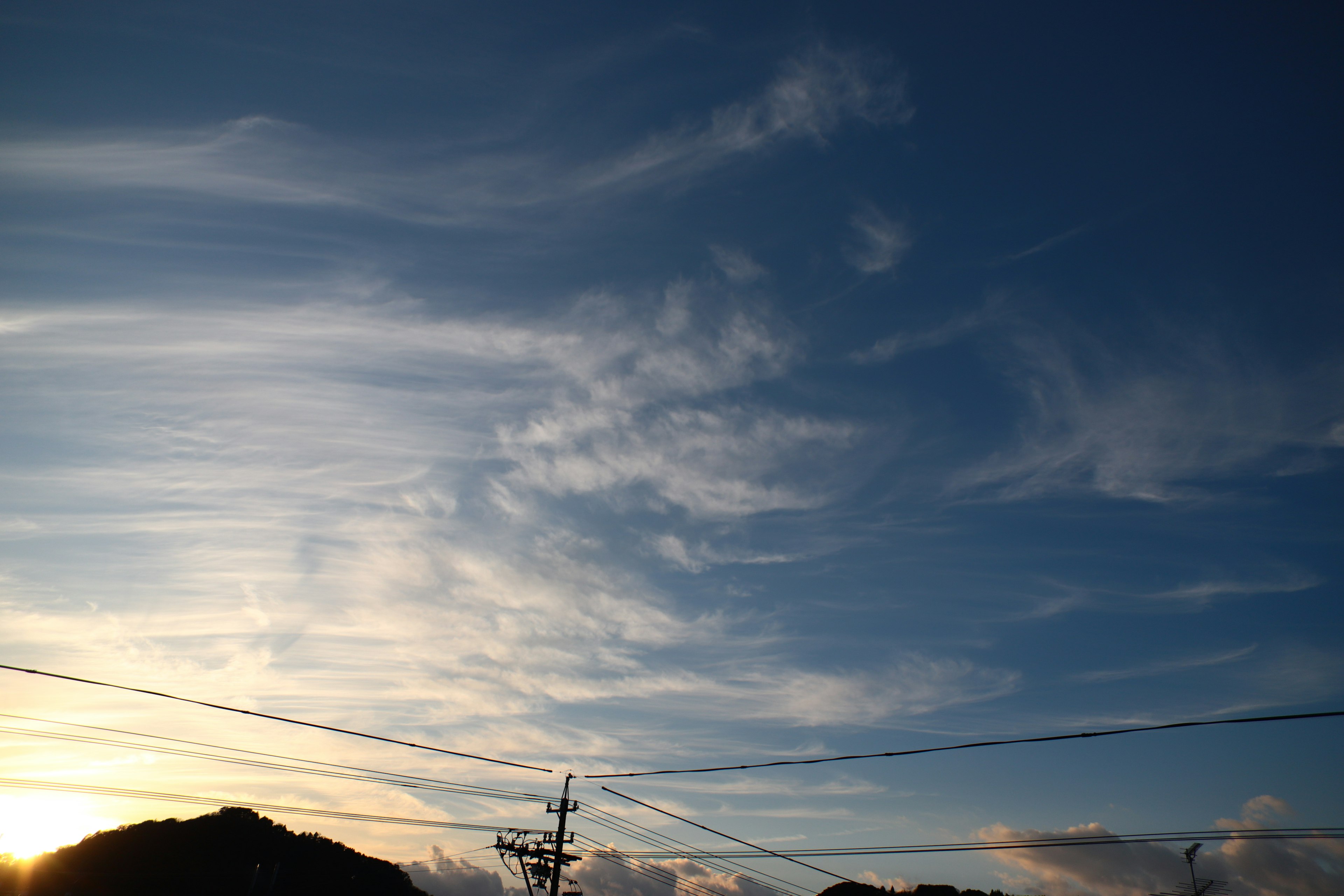 Blauer Himmel mit zarten weißen Wolken und Blick auf den Sonnenuntergang