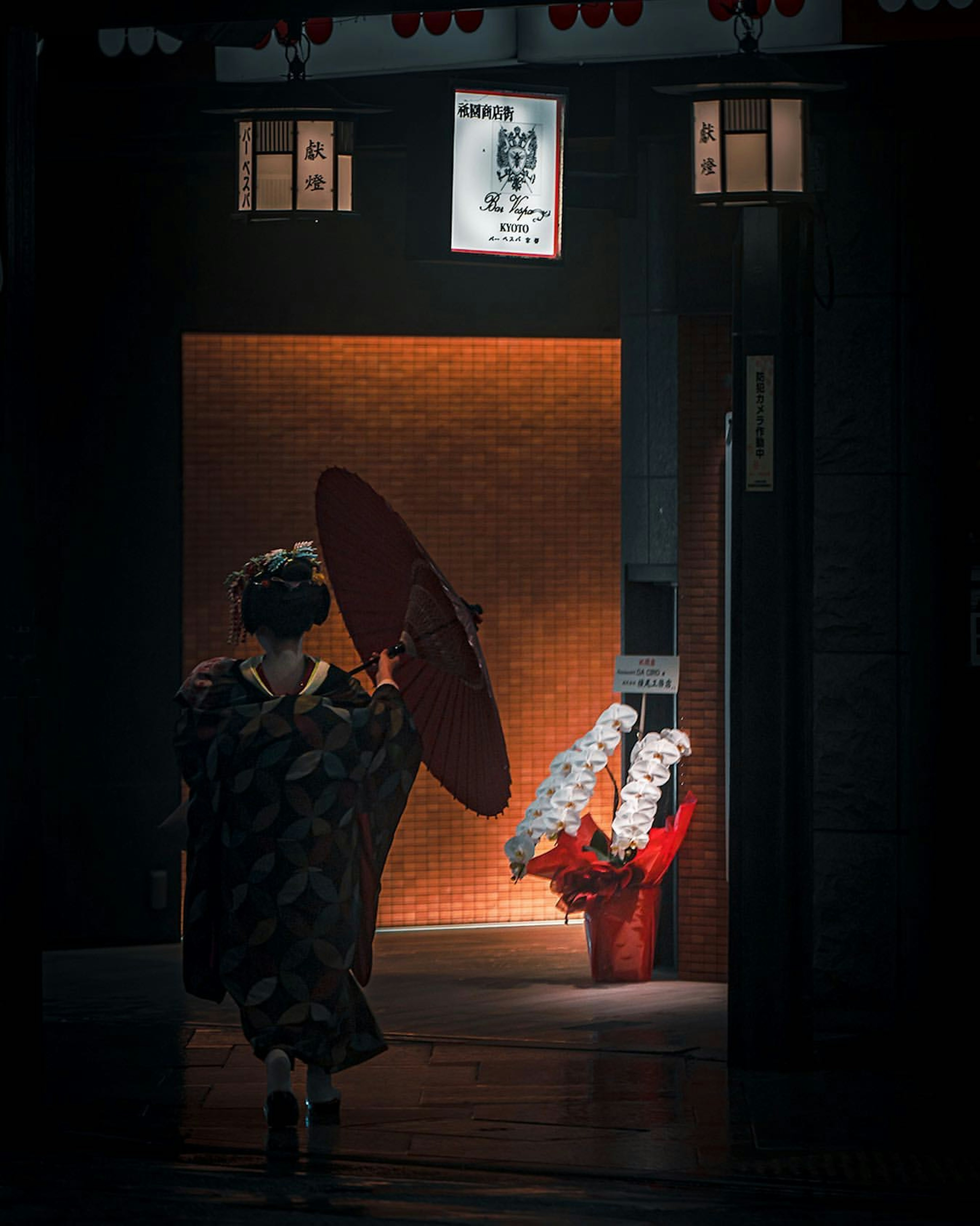 Frau im traditionellen Kimono mit einem roten Regenschirm und einem hellen Eingang im Hintergrund